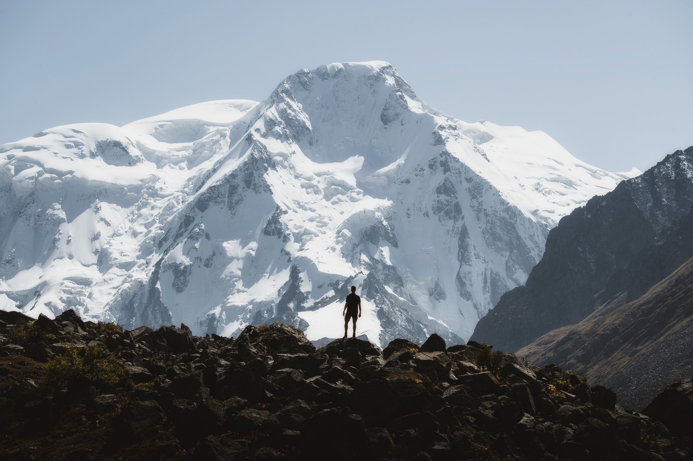 Hiker silhouetted before a towering snowy massif