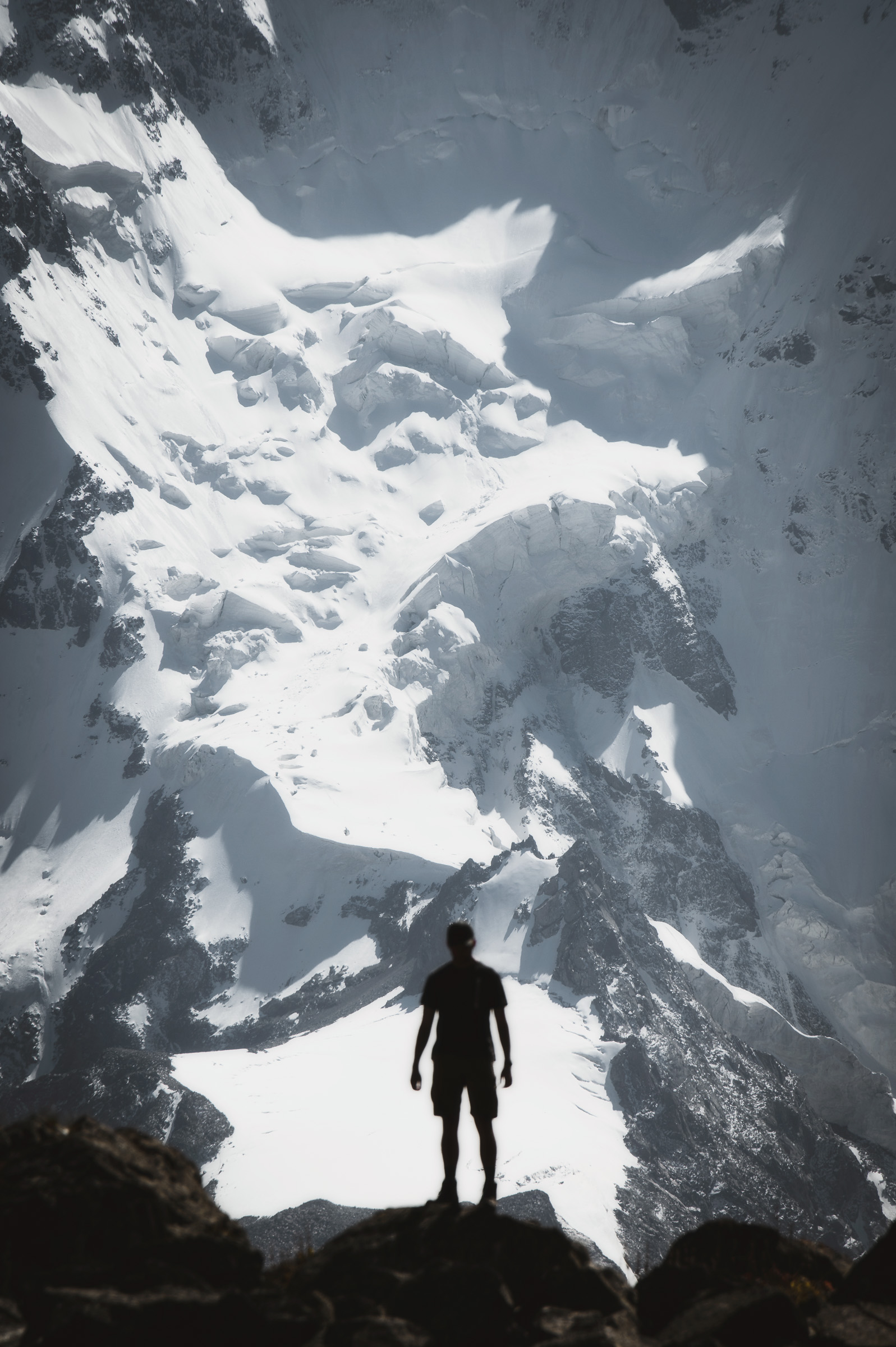 Hiker on a rocky ridge beneath a massive white mountain