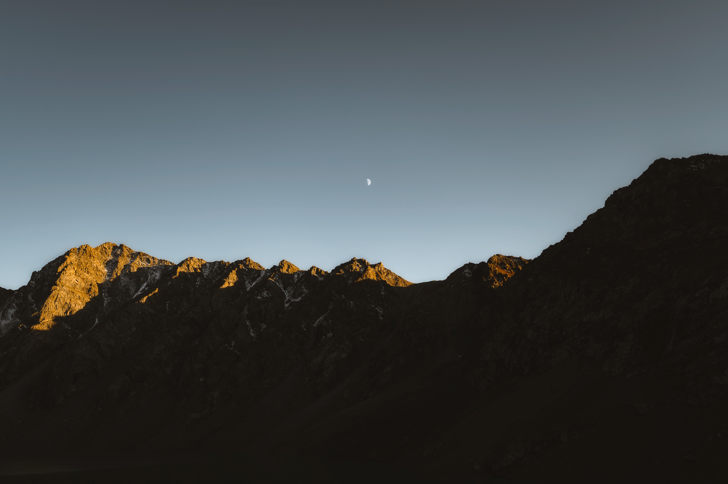 Small moon above a shadowed mountain ridge at dusk