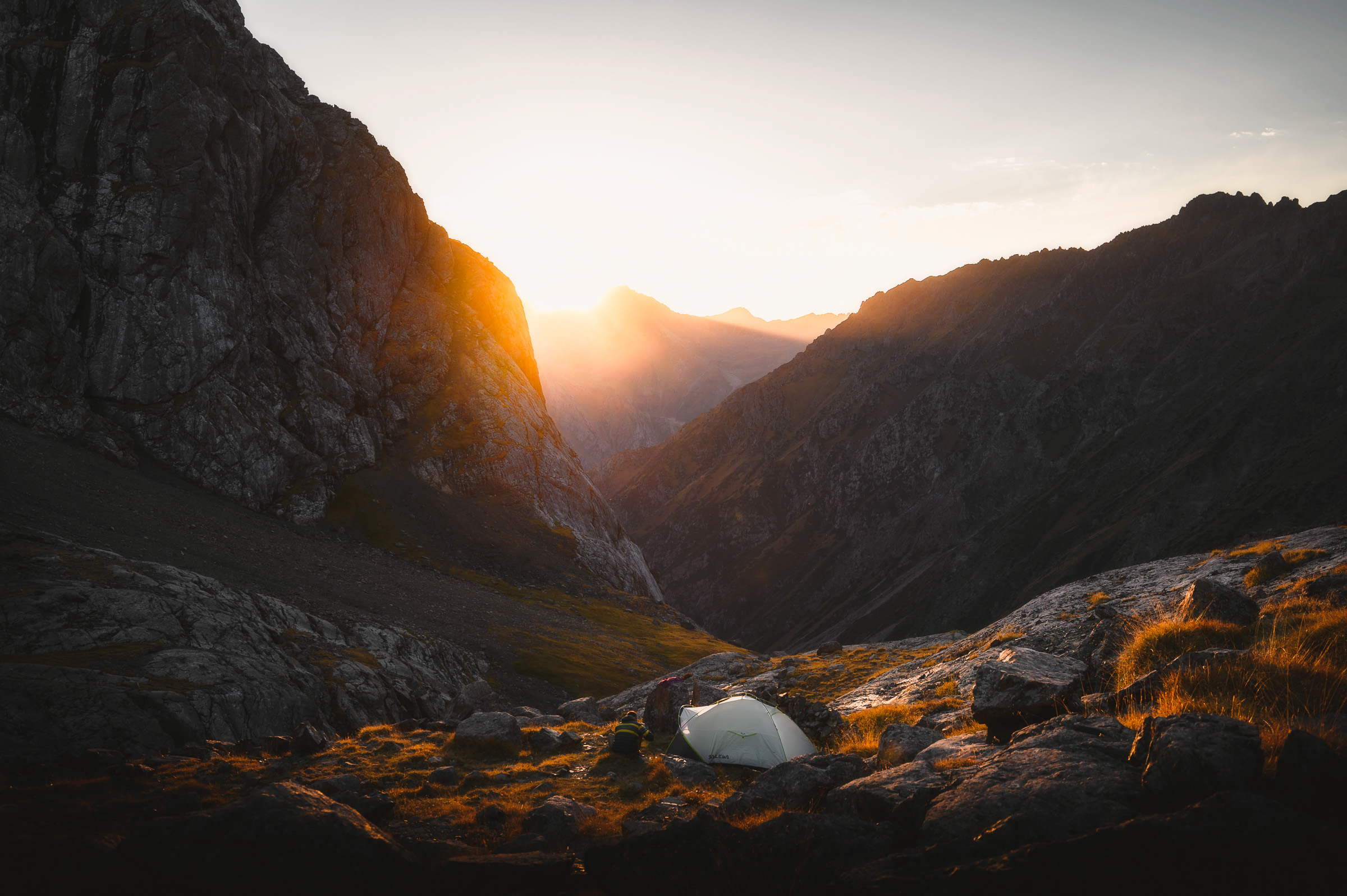 Tent on rocky ground as sunrise enters a mountain valley