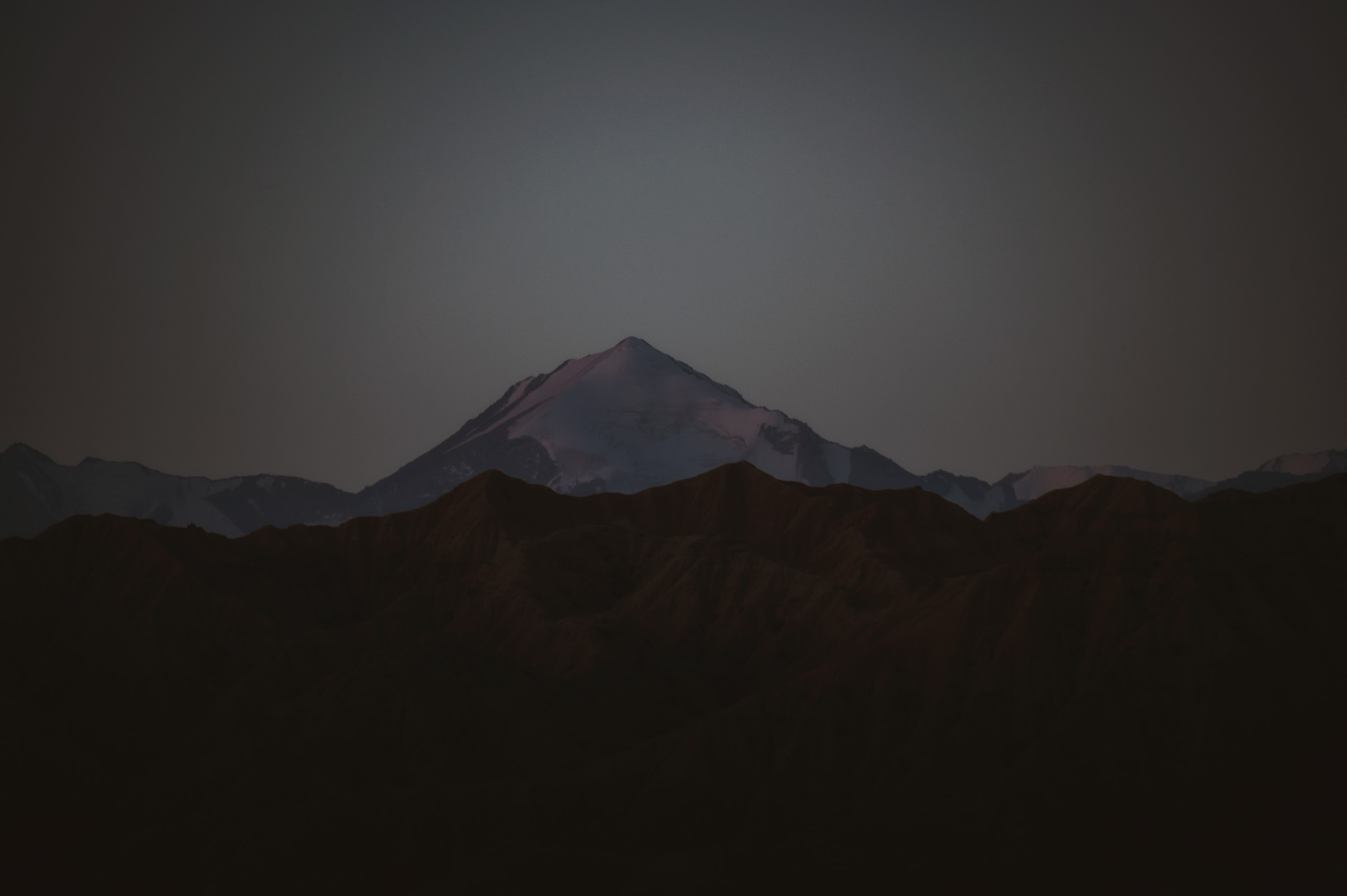 Snow-capped peak visible beyond dark hills after sunset