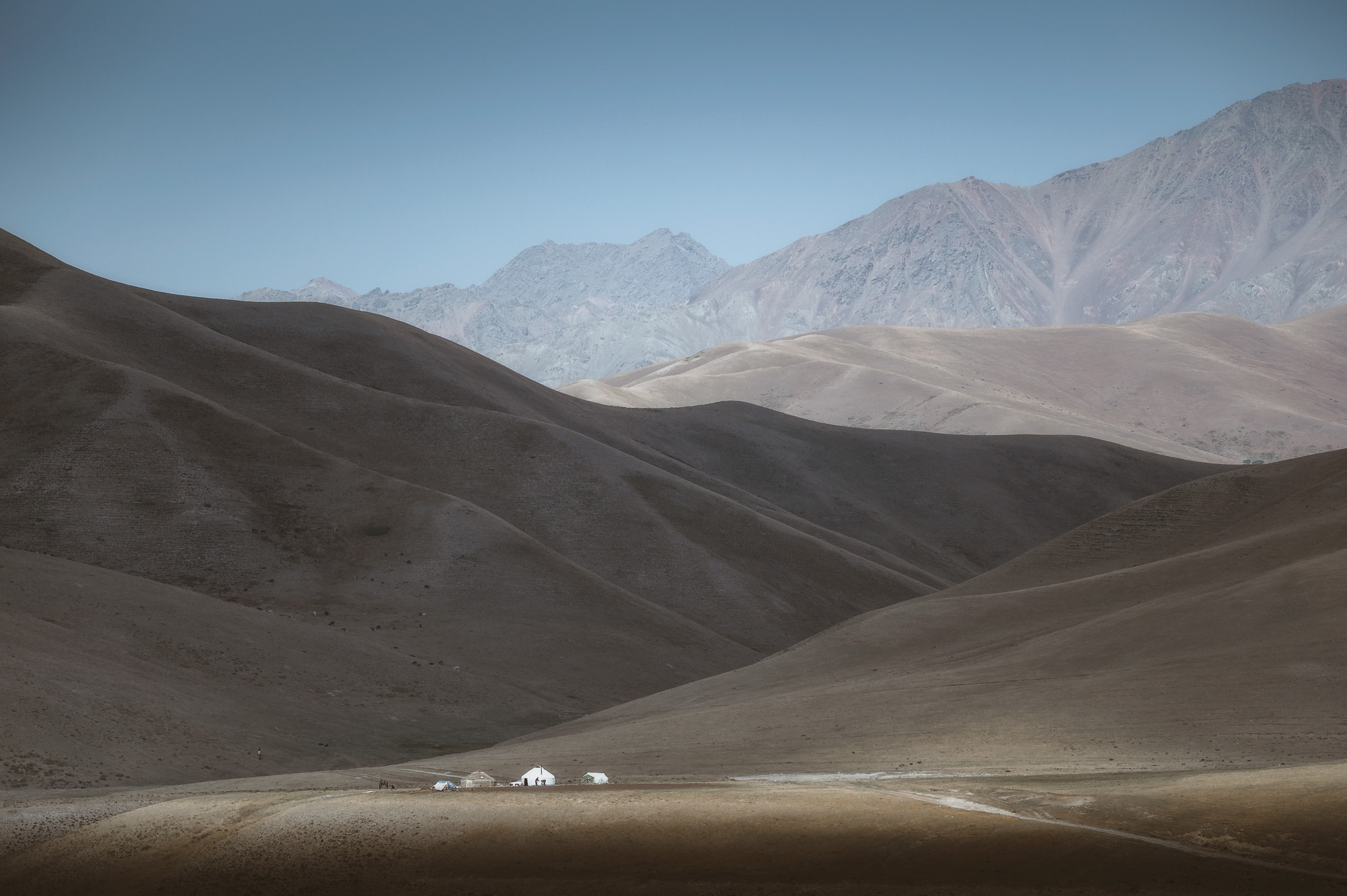 Smooth gray hills with distant mountains under a clear sky
