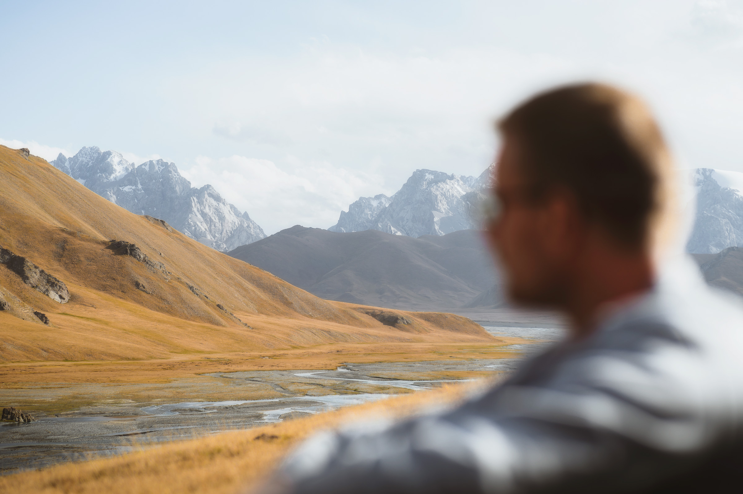 Traveler looking across a river toward a snowy mountain range