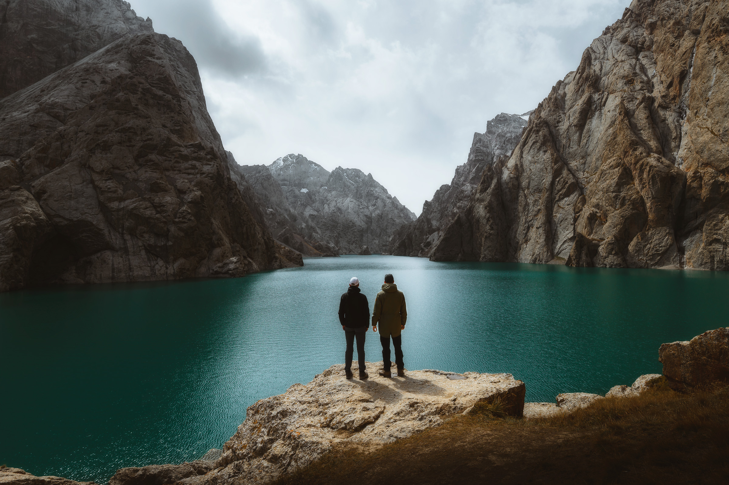 Two travelers standing on a rock above a turquoise canyon lake