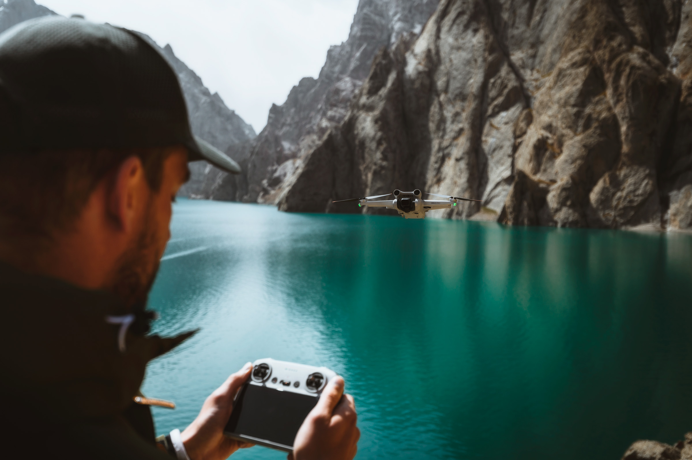 Photographer flying a drone beside a turquoise mountain lake