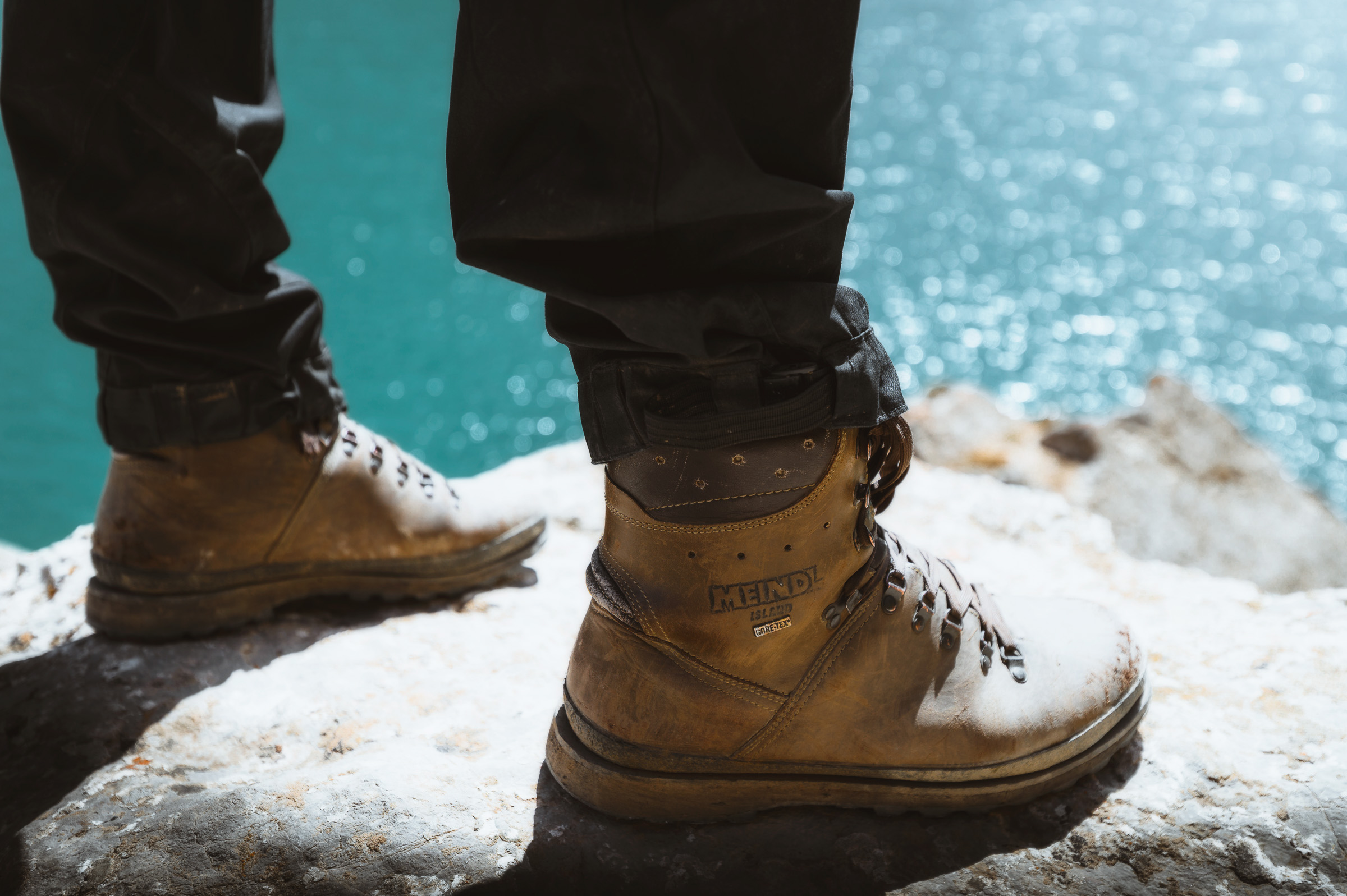 Hiking boots on a snowy ledge above turquoise water
