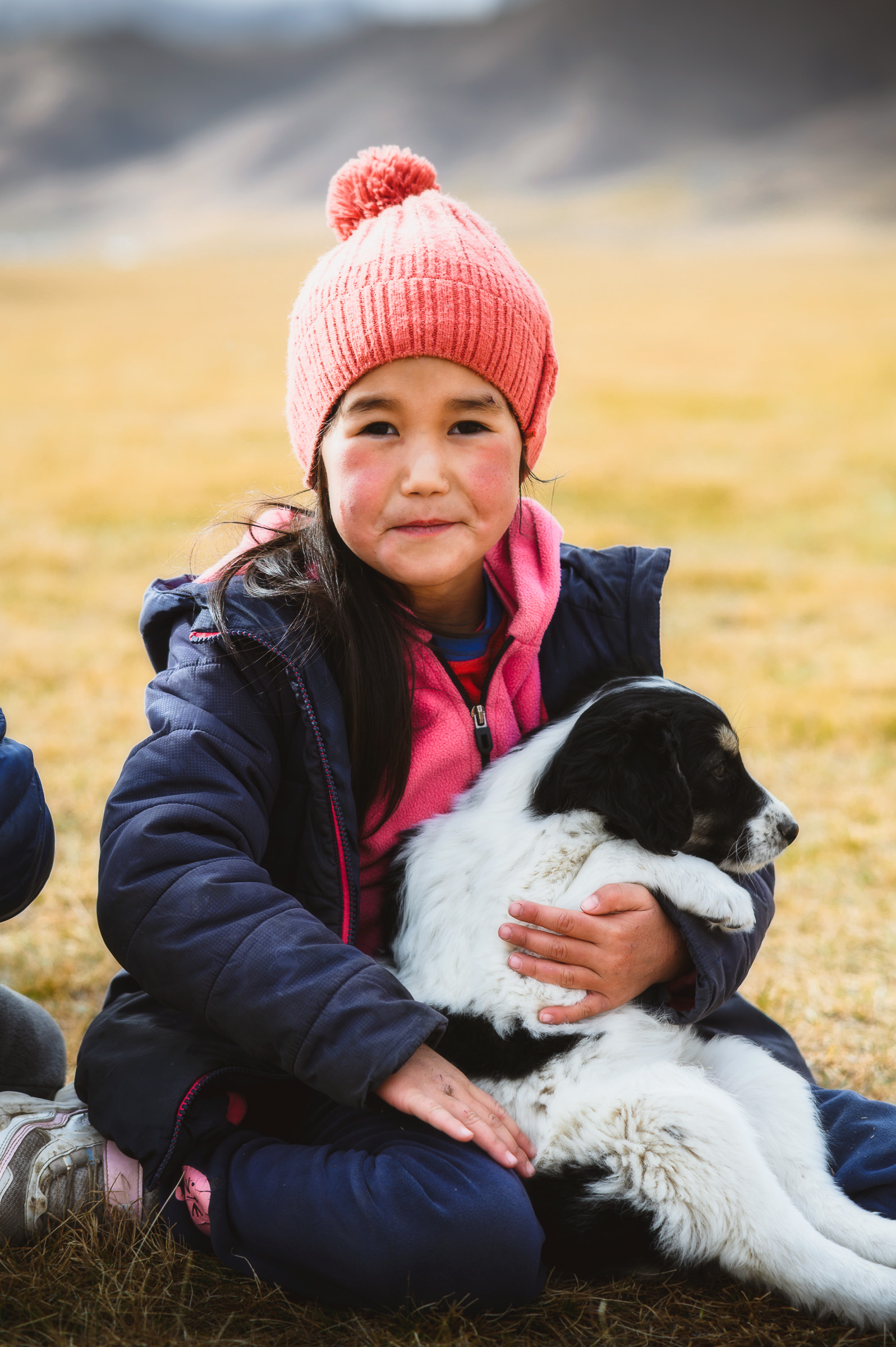 Young child in a pink hat holding a black-and-white puppy