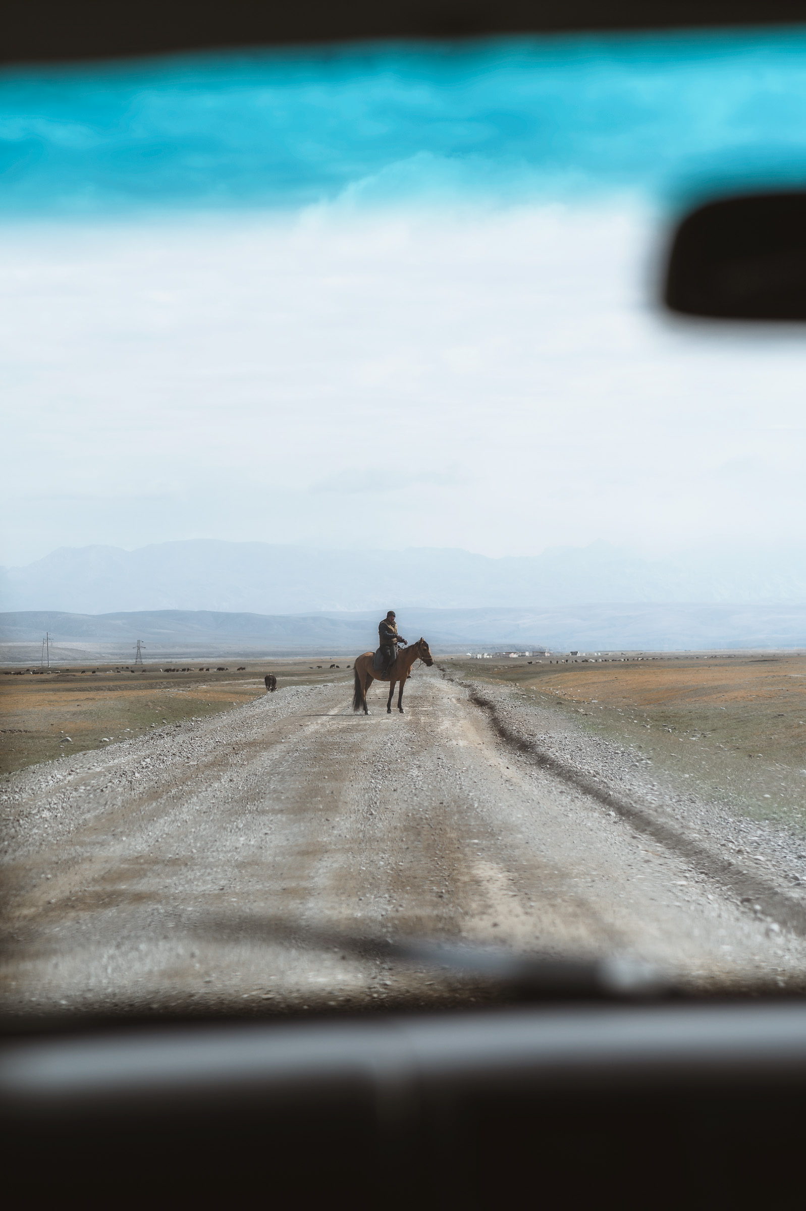 Distant horseman on a gravel road seen through a windshield