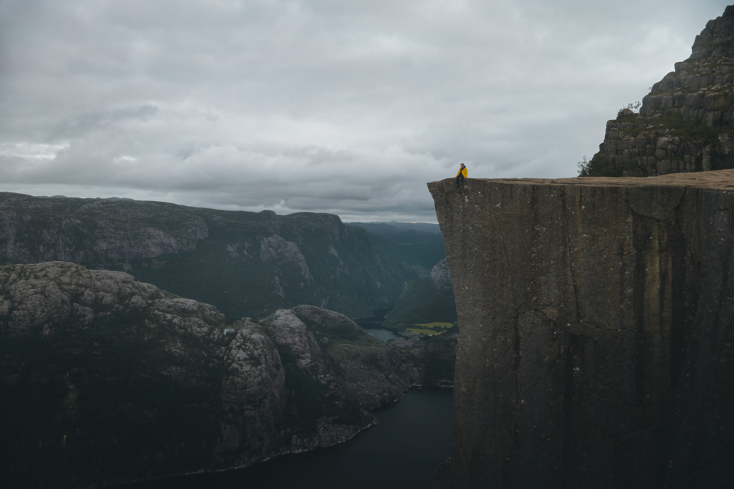 Hiker in a yellow jacket on Preikestolen above the dark fjord