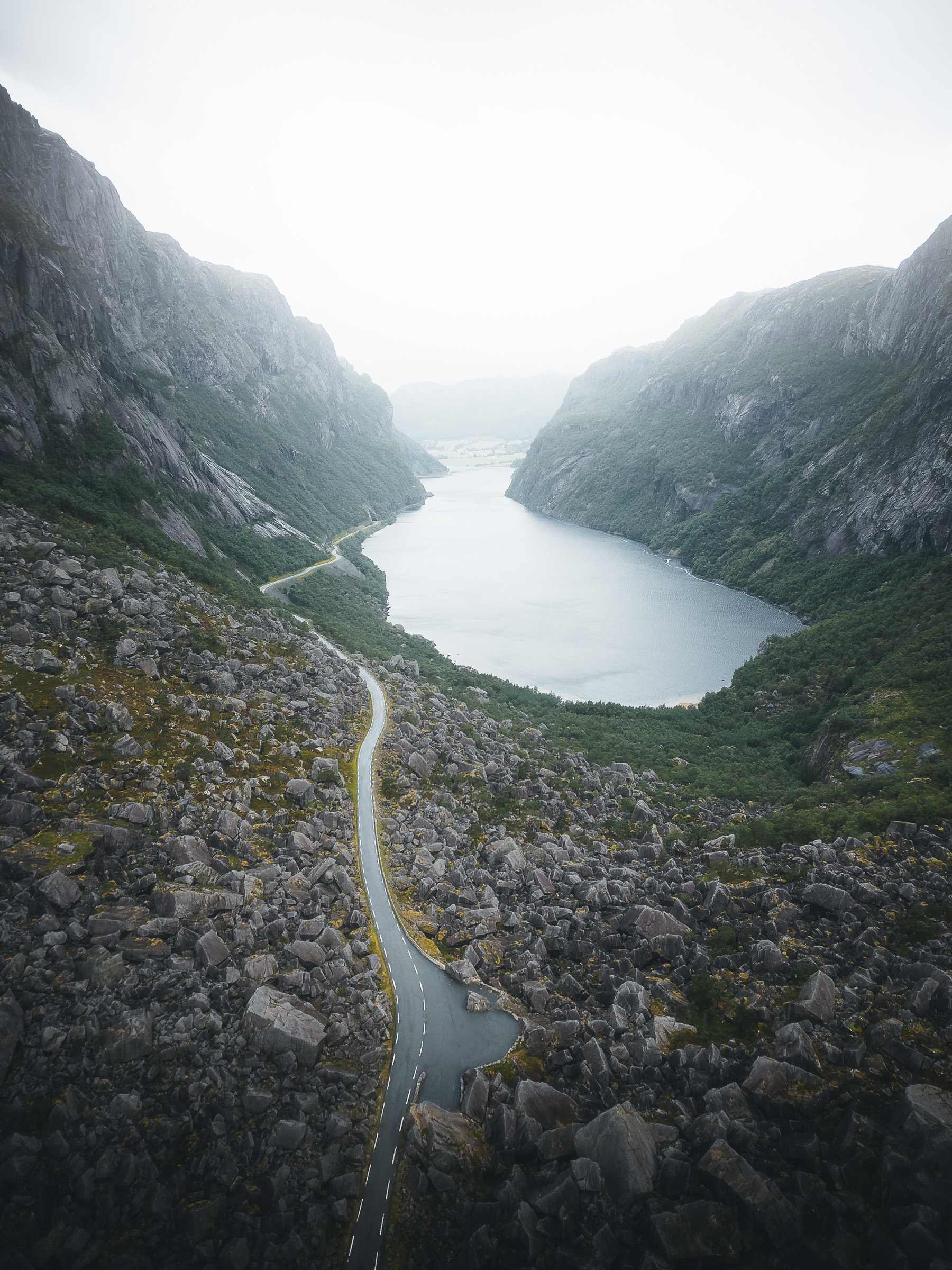 Narrow road winding beside a fjord between steep mountains