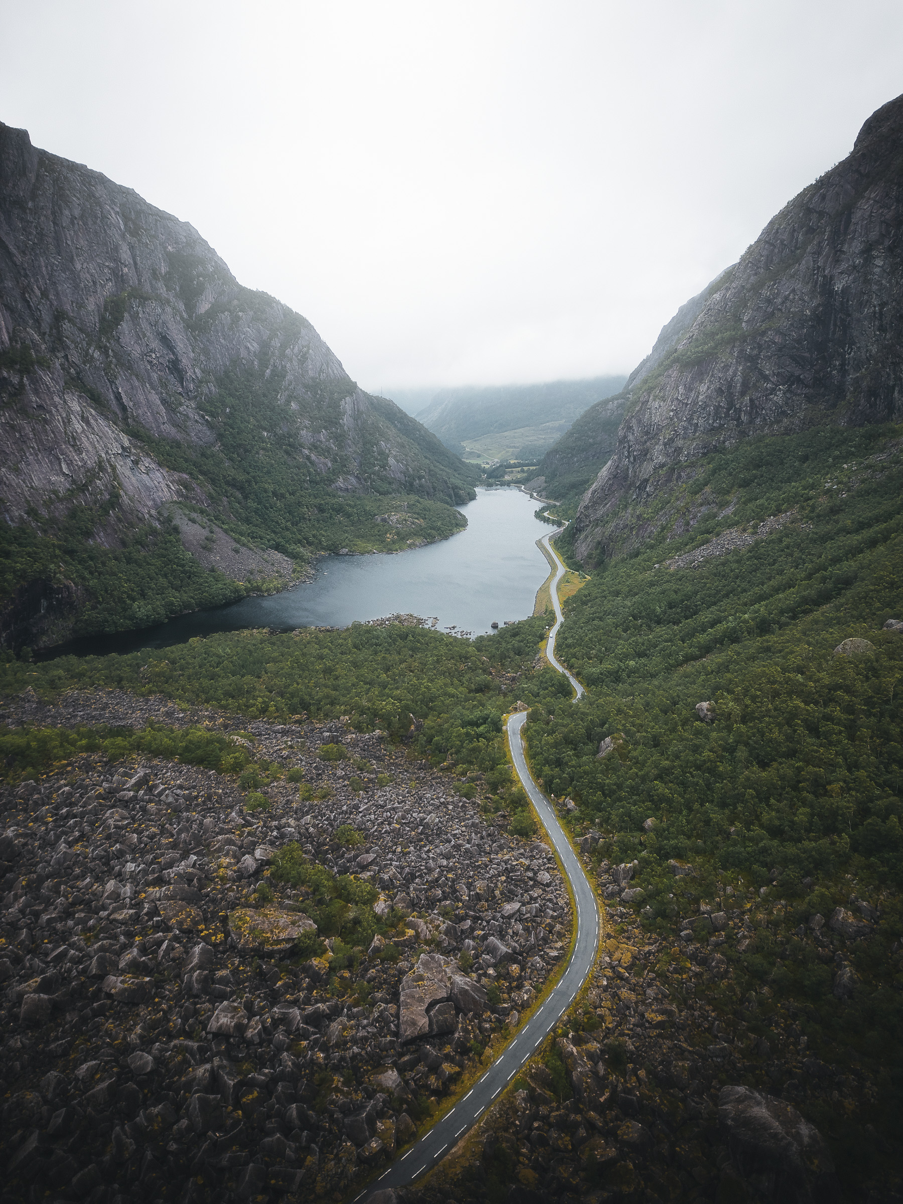 Aerial view of a winding road beside a narrow mountain lake