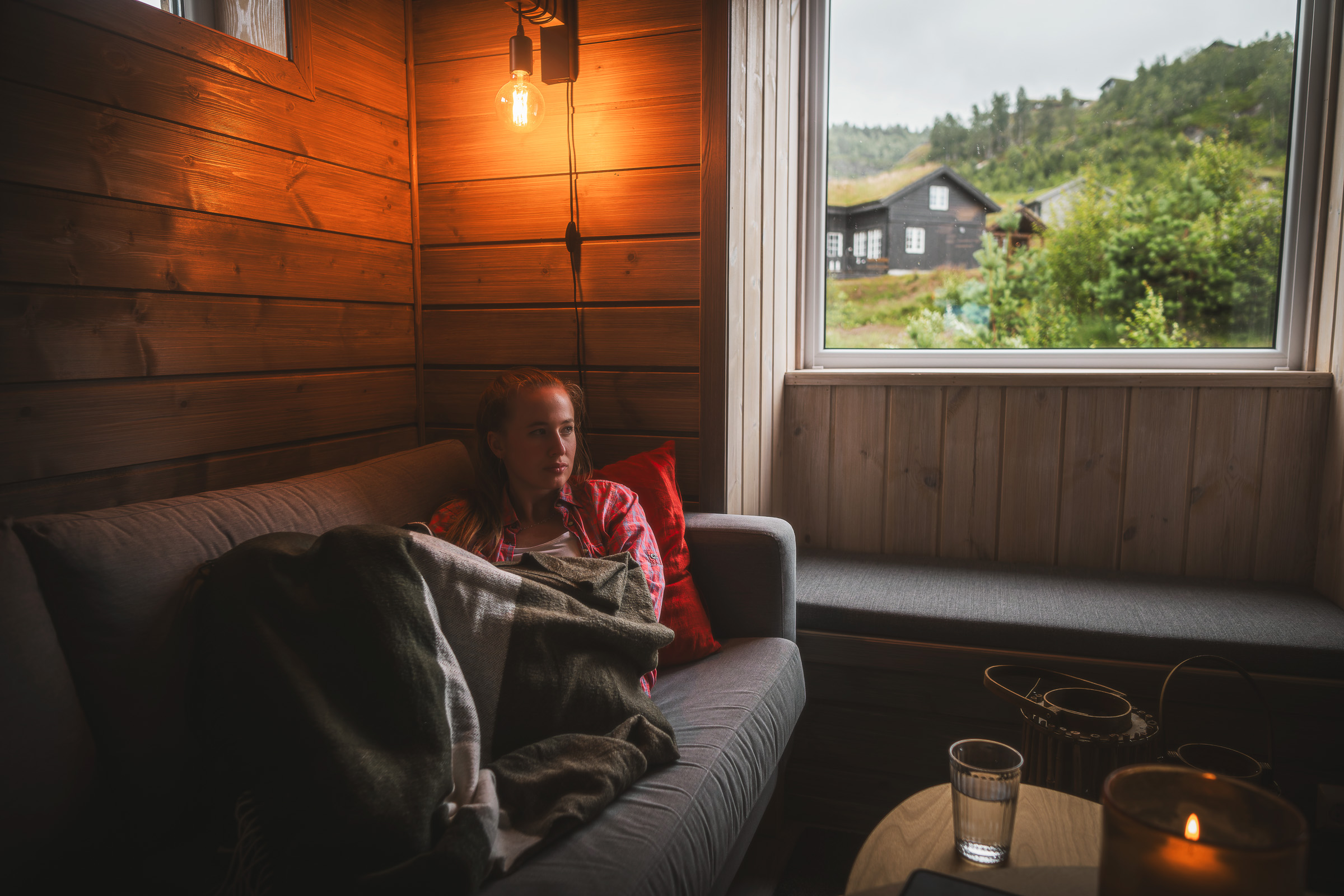 Woman resting inside a wooden cabin while rain falls outside