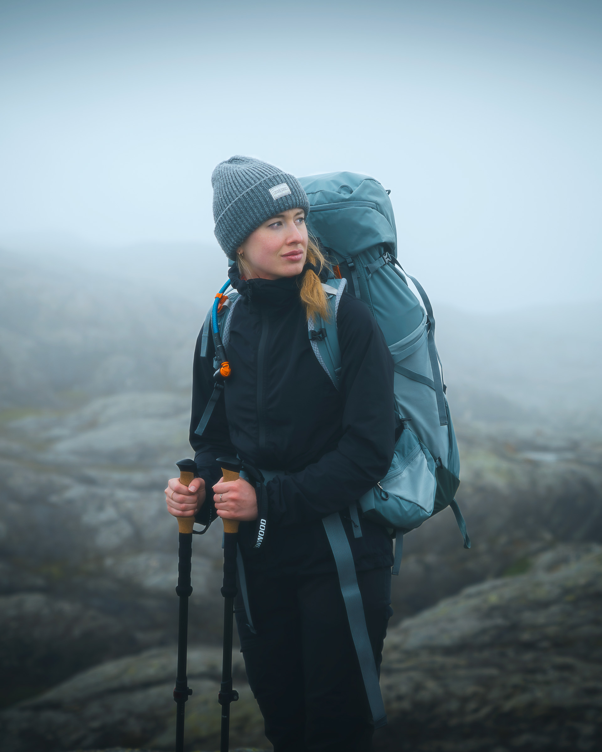 Woman hiker with trekking poles and a large backpack in the mist