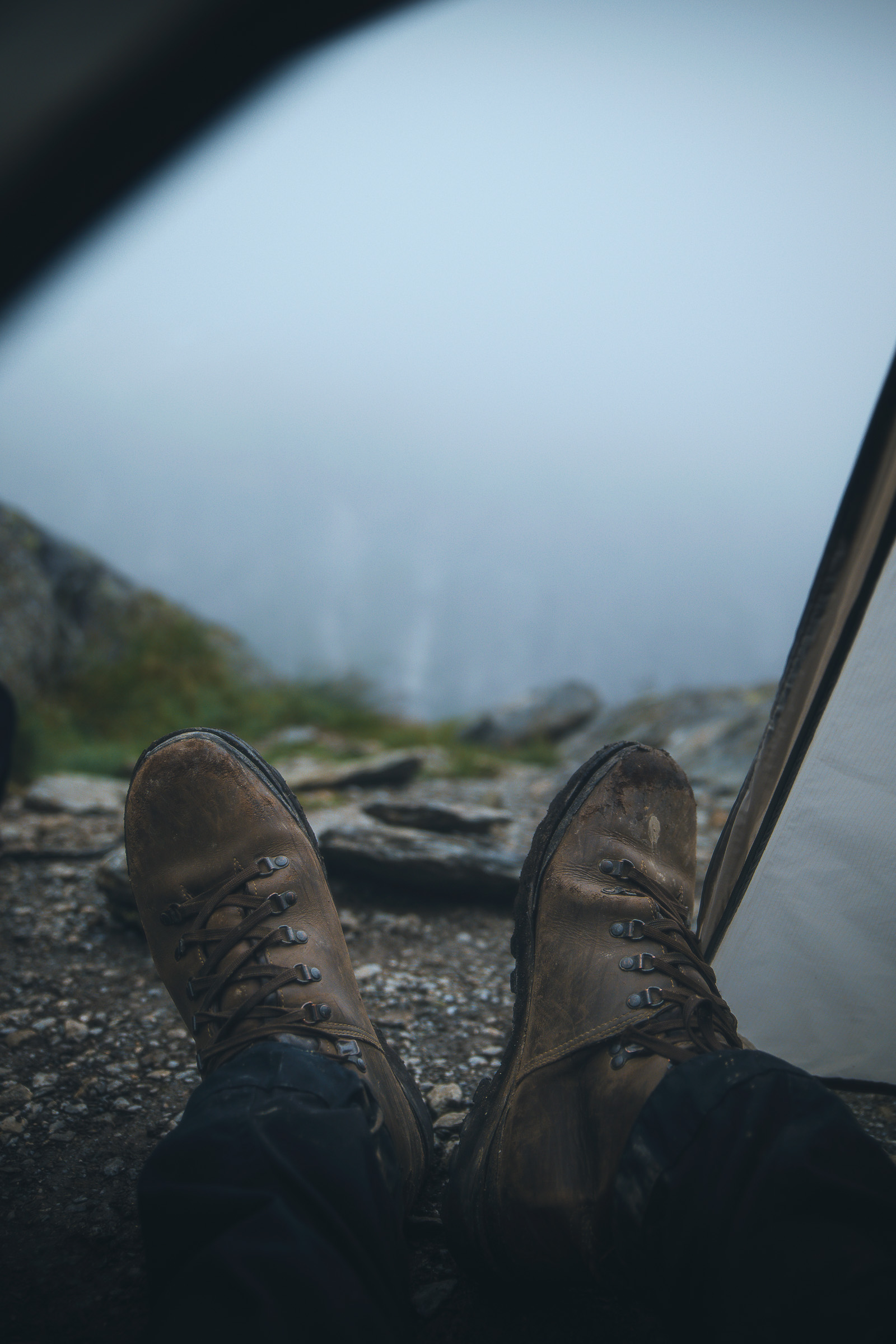Muddy hiking boots inside a tent overlooking a cloudy valley