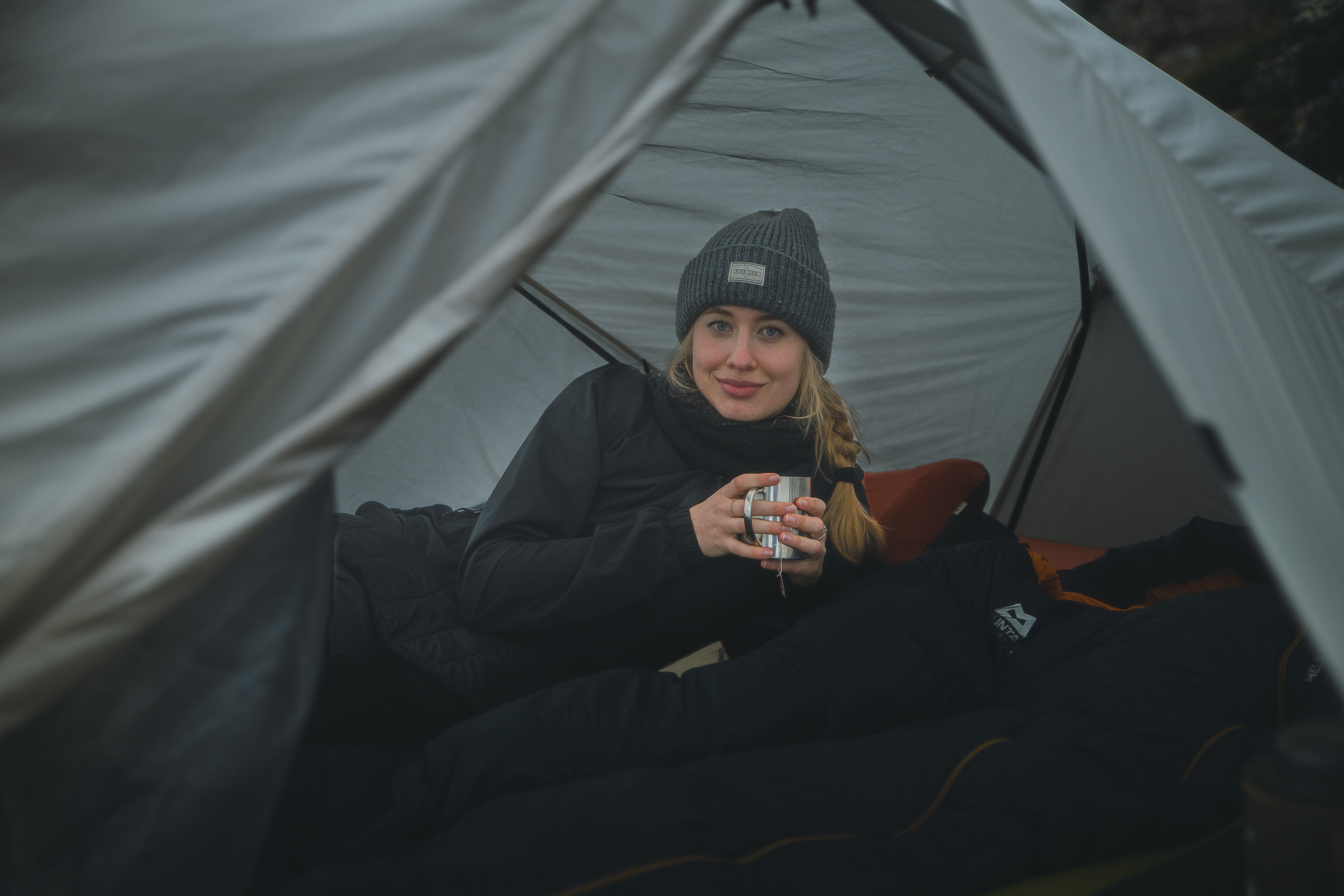 Woman holding a metal mug while sitting inside a tent