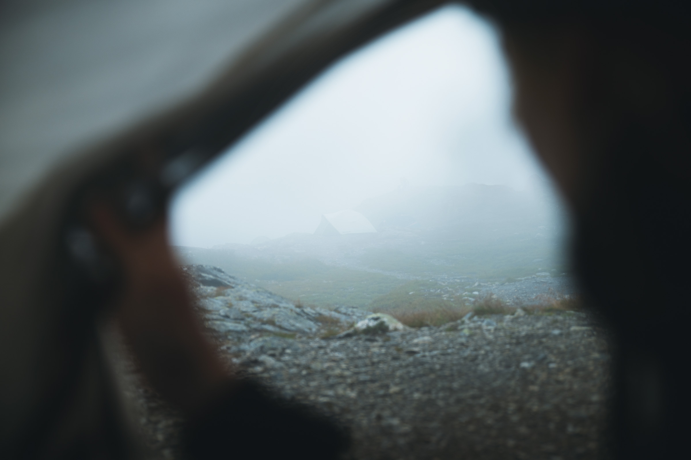 Rainy mountain plateau seen through the opening of a tent