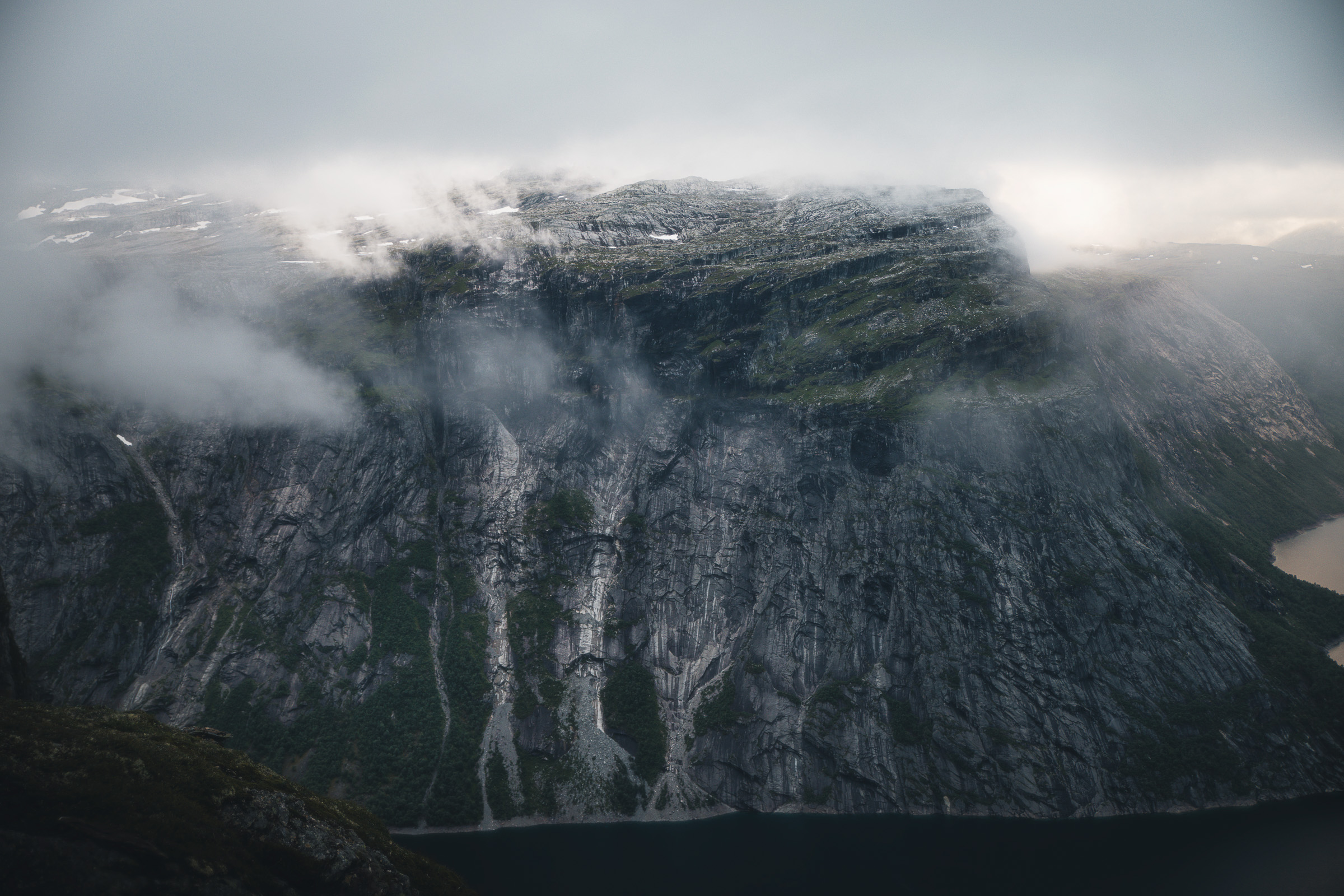 Waterfalls descending cliffs into a mountain lake under low clouds