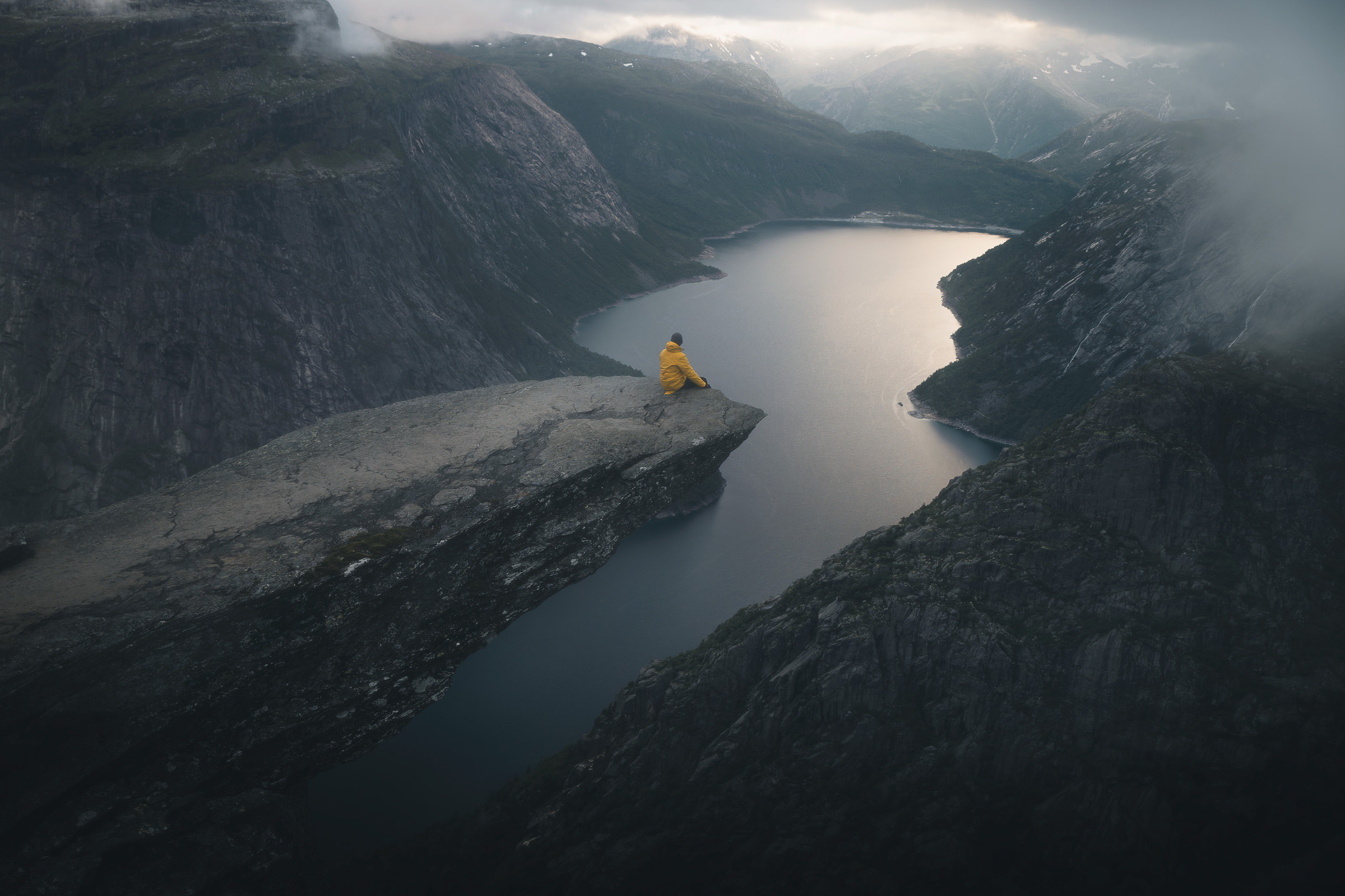 Hiker in a yellow jacket standing on Trolltunga above Ringedalsvatnet