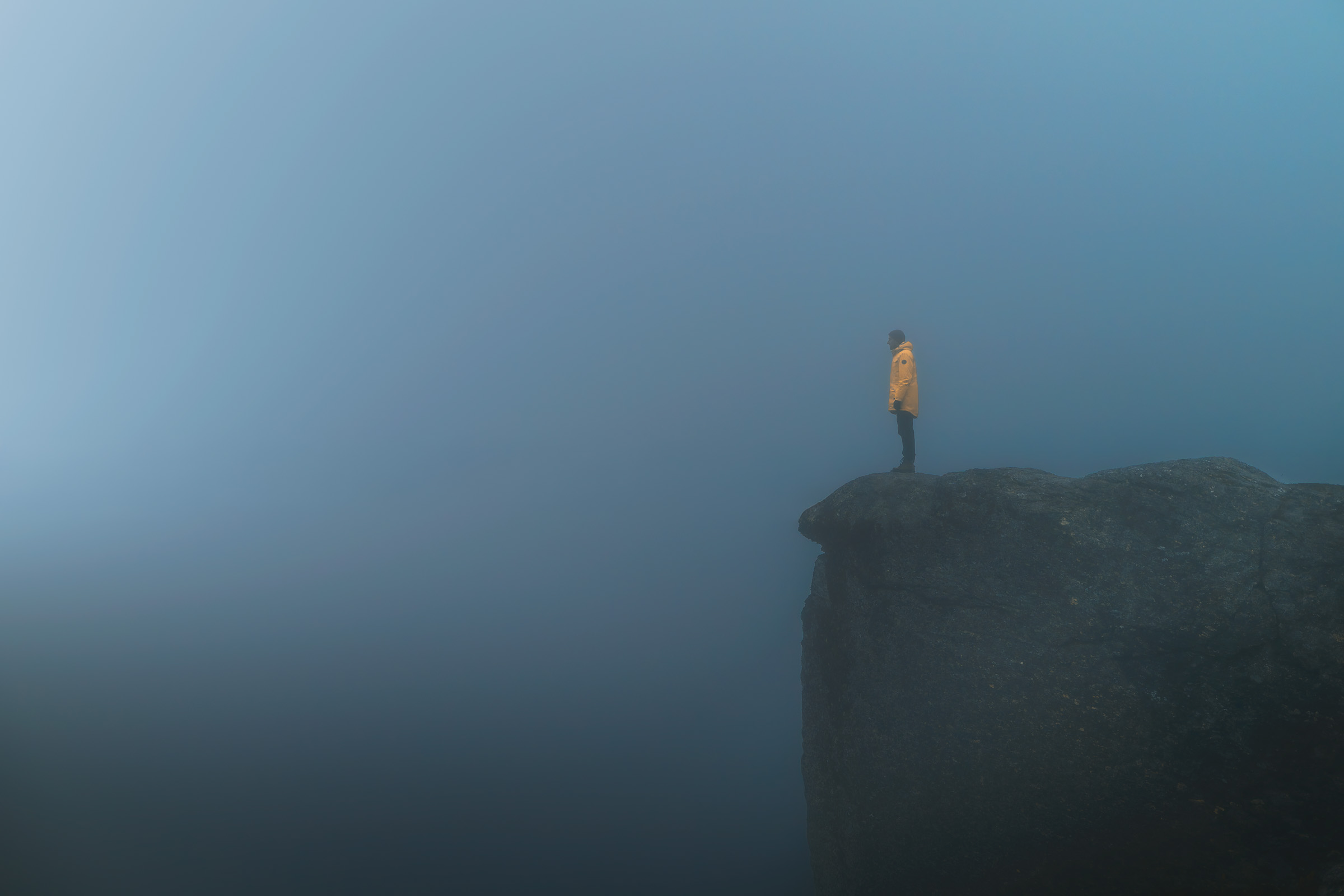 Hiker in a yellow jacket on a rock ledge in dense fog