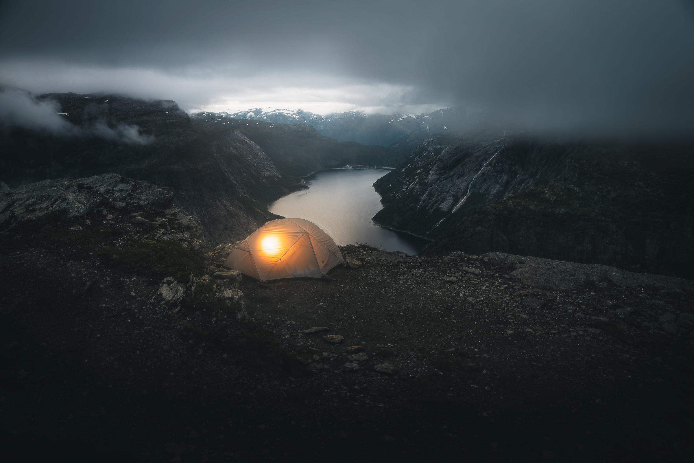 Glowing tent on a rocky ridge overlooking a mountain lake