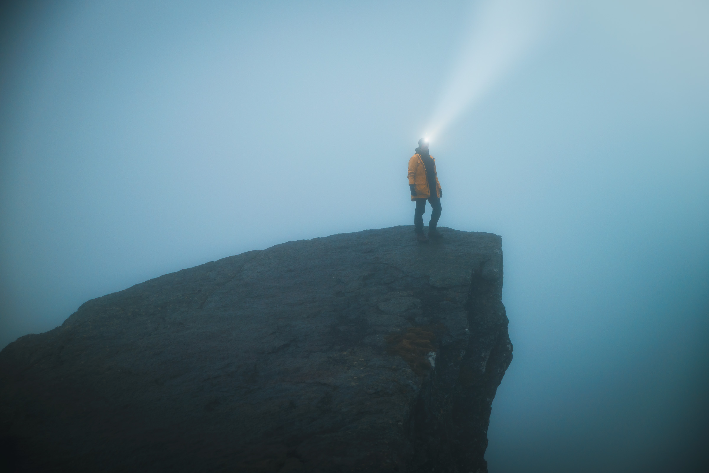 Hiker casting a headlamp beam from a rock ledge in thick fog