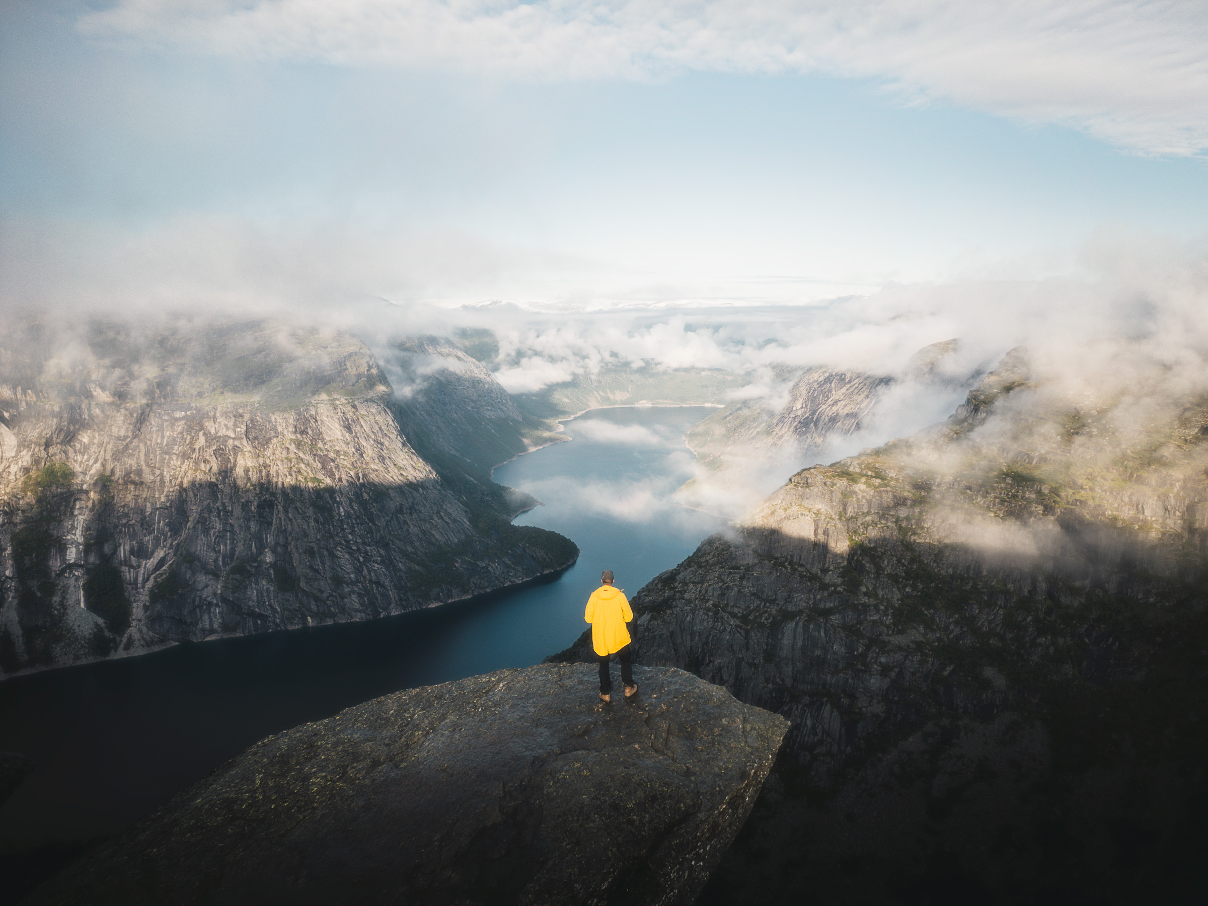 Hiker in a yellow jacket above Ringedalsvatnet as clouds begin to lift