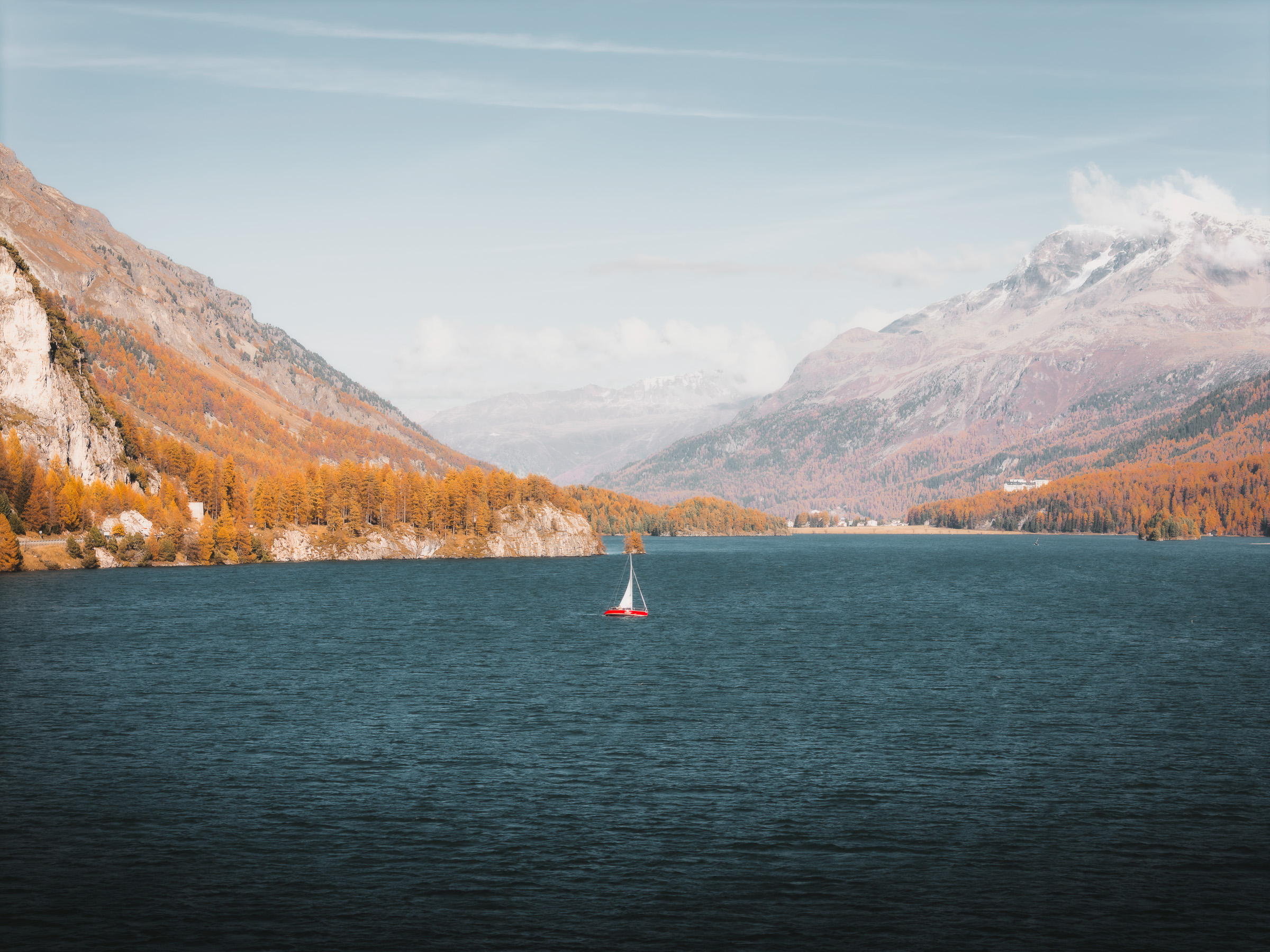 Small sailboat crossing an alpine lake beneath snowy peaks