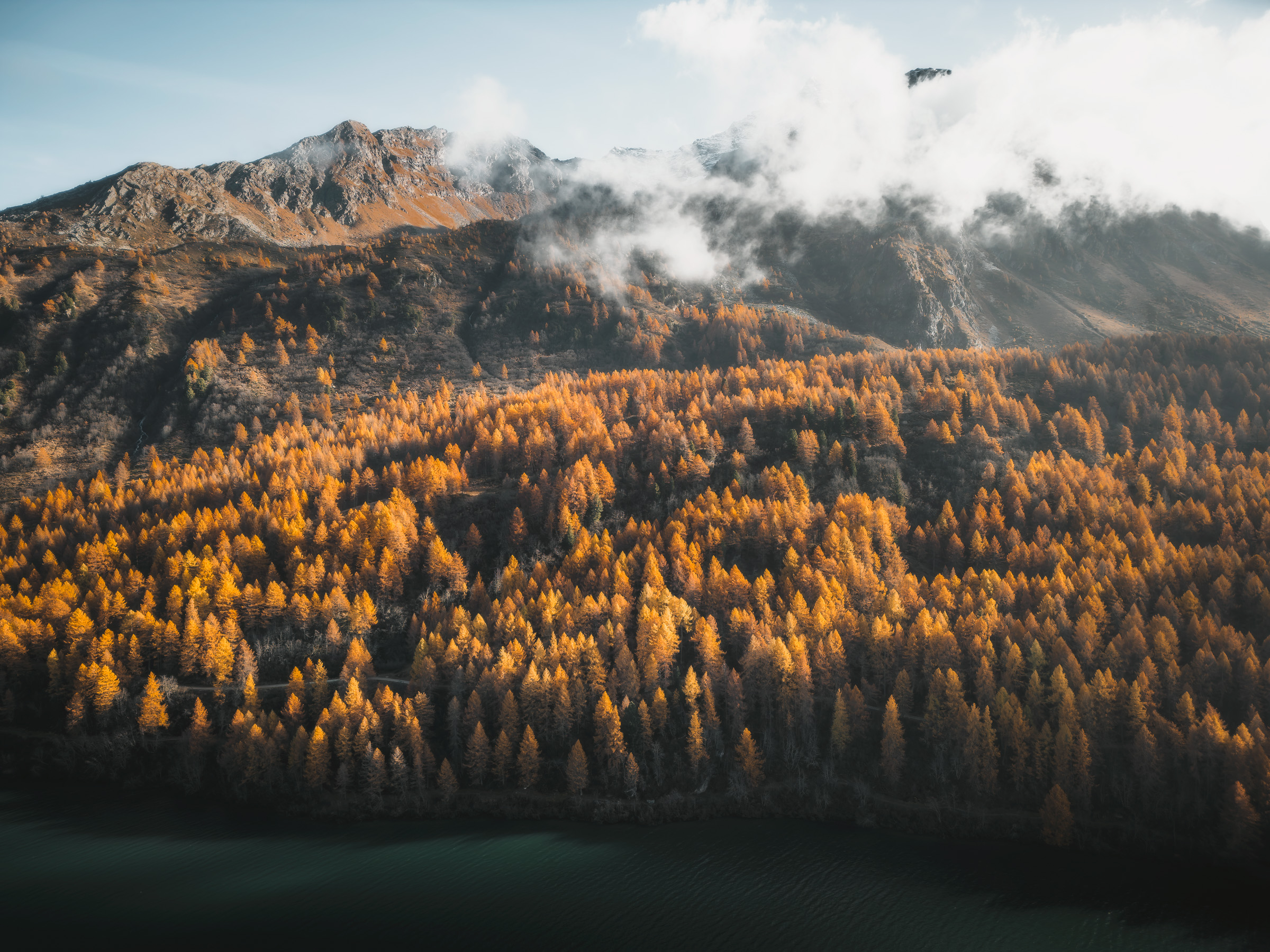 Low clouds drifting across a mountain above golden larches