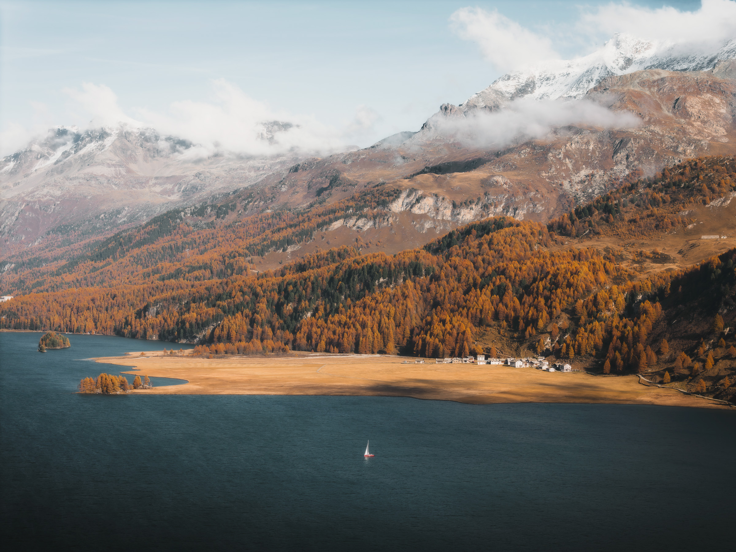 Aerial view of Lake Sils, autumn shoreline and a lone sailboat