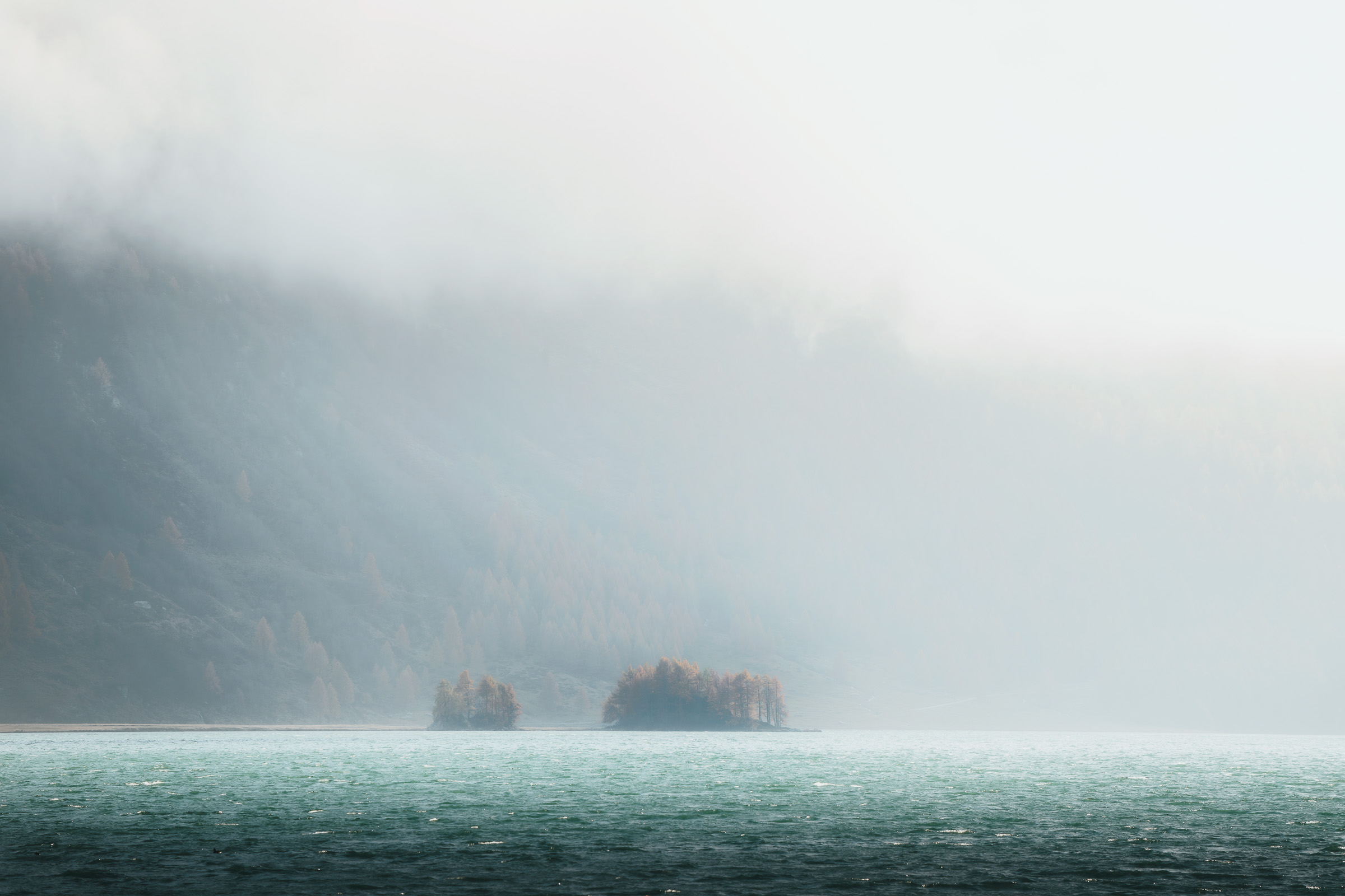 Small wooded islands fading into mist on an alpine lake