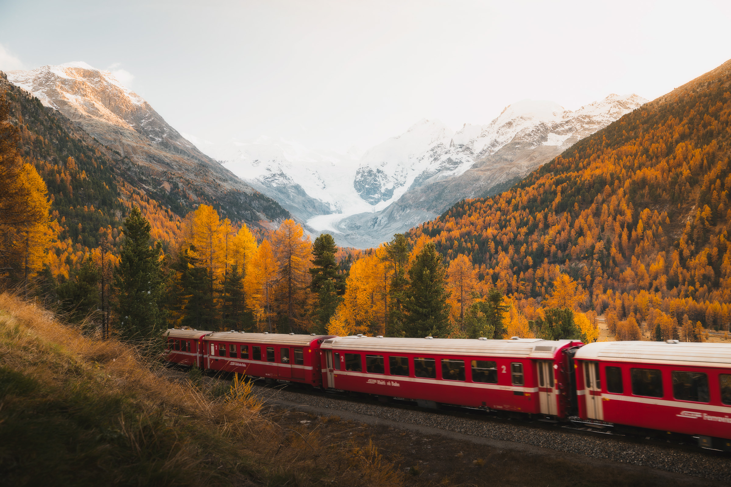Red Rhaetian Railway train crossing an autumn alpine valley
