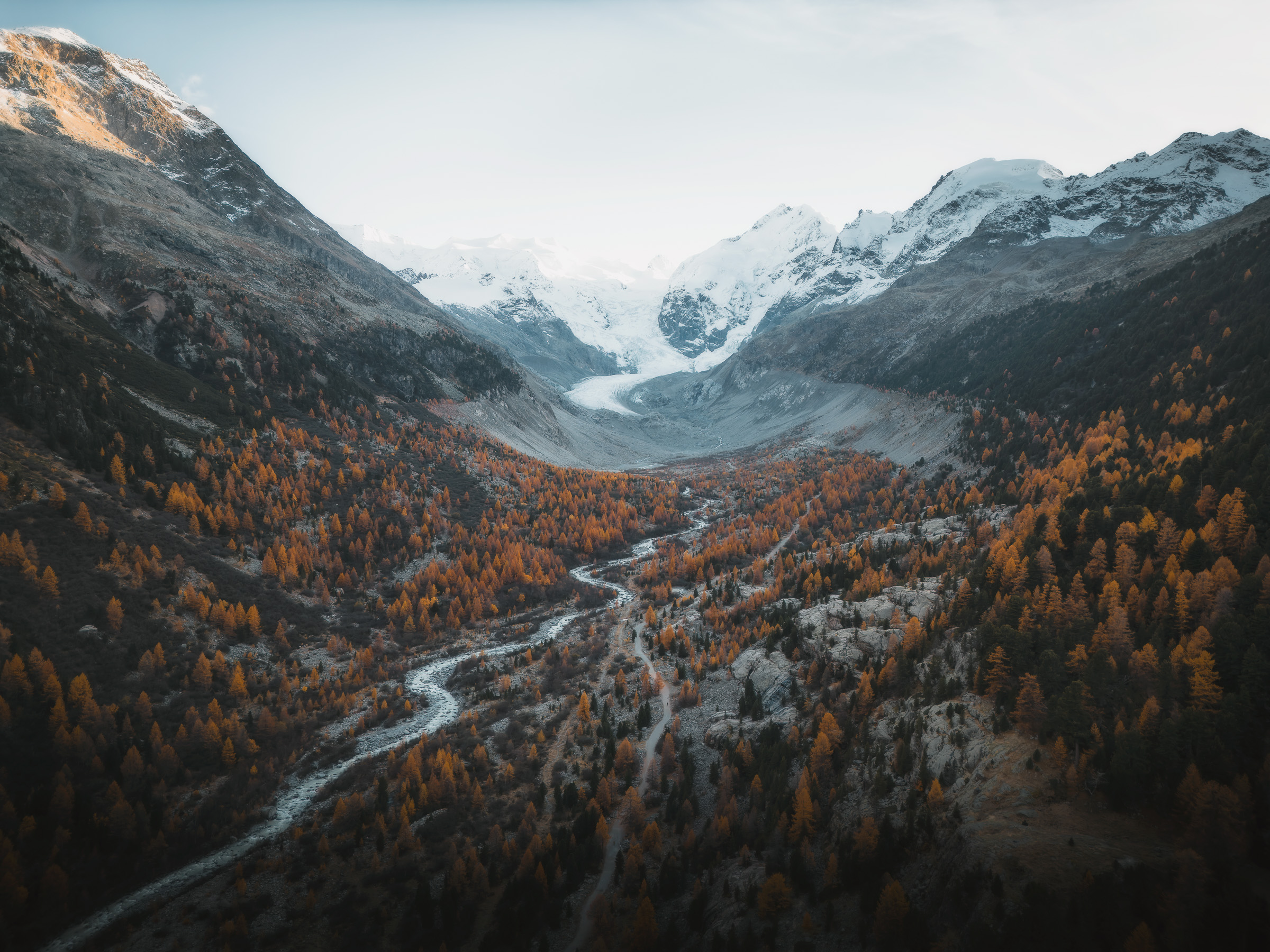 Glacier valley and winding river surrounded by autumn larches