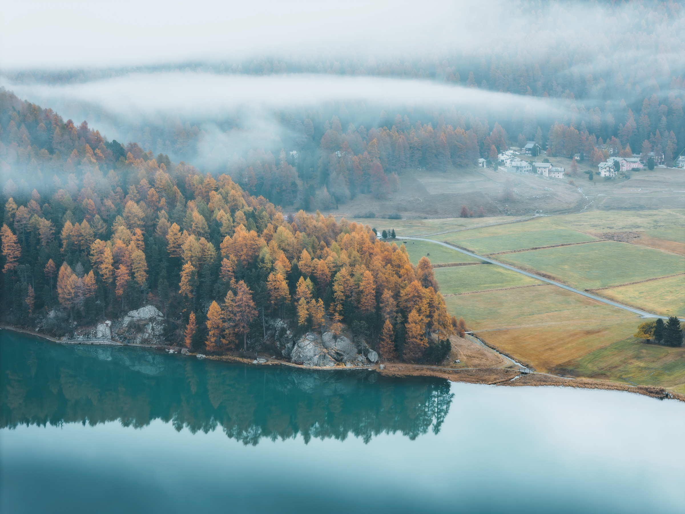 Aerial view of a turquoise lake, fields and autumn larches