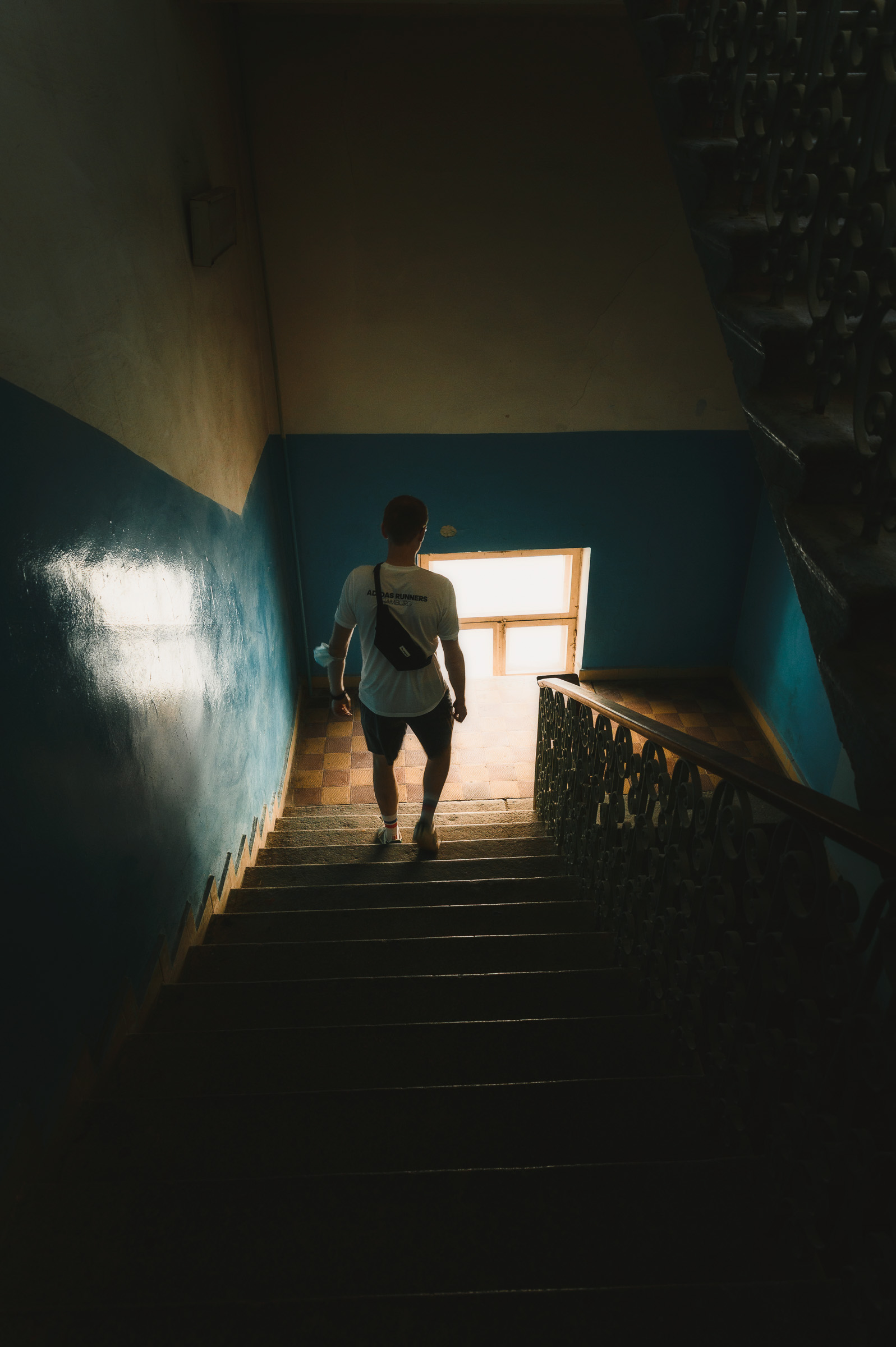 Person climbing a dim stairwell toward a sunlit window