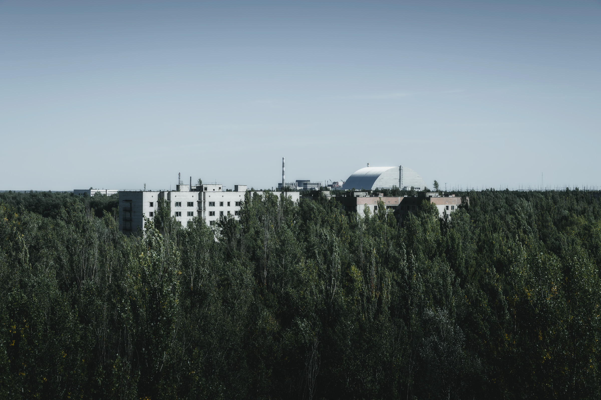 Chernobyl reactor shelter visible beyond forest and abandoned buildings