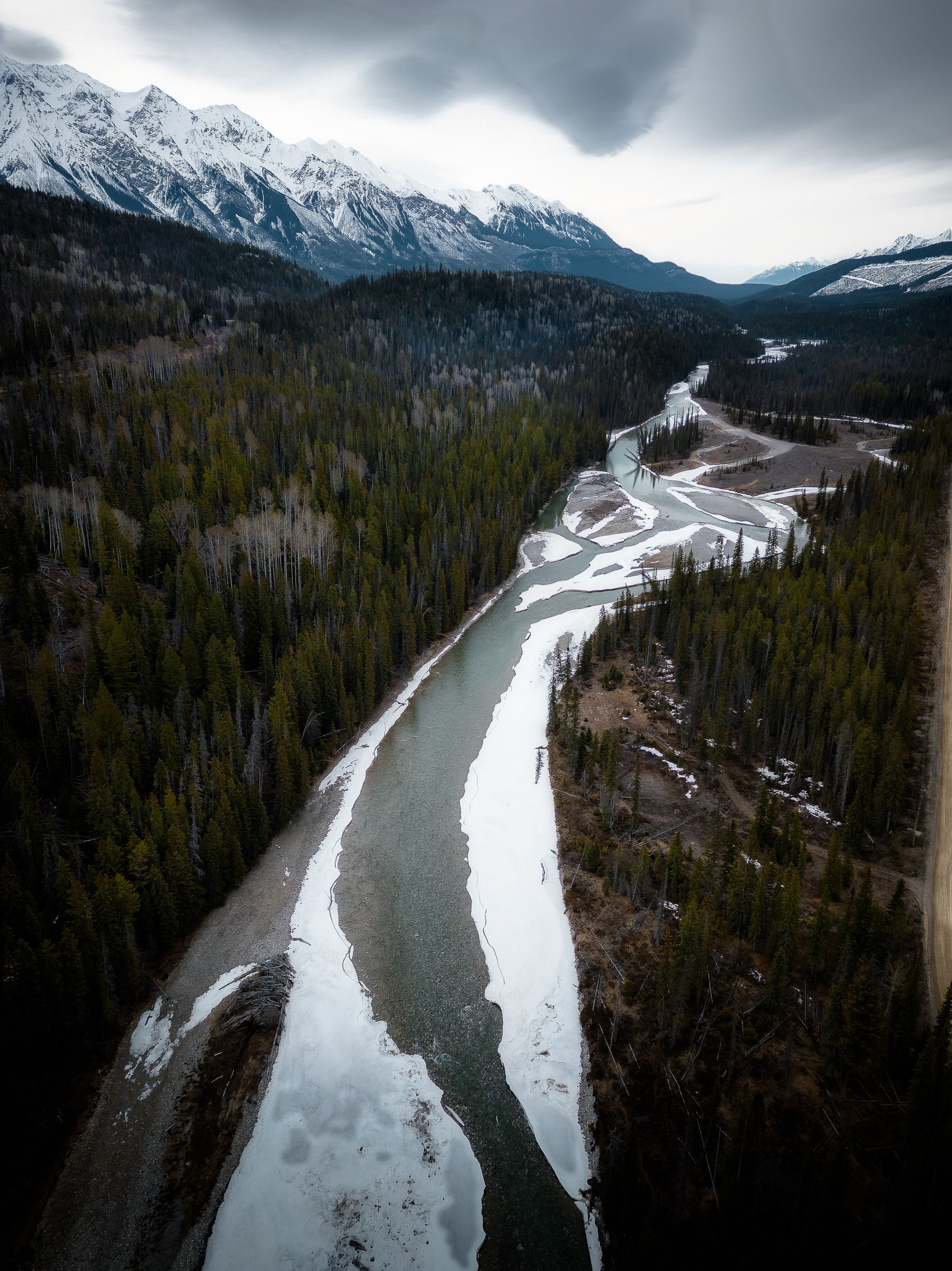 Aerial view of a winding river beneath snowy mountains in Canada