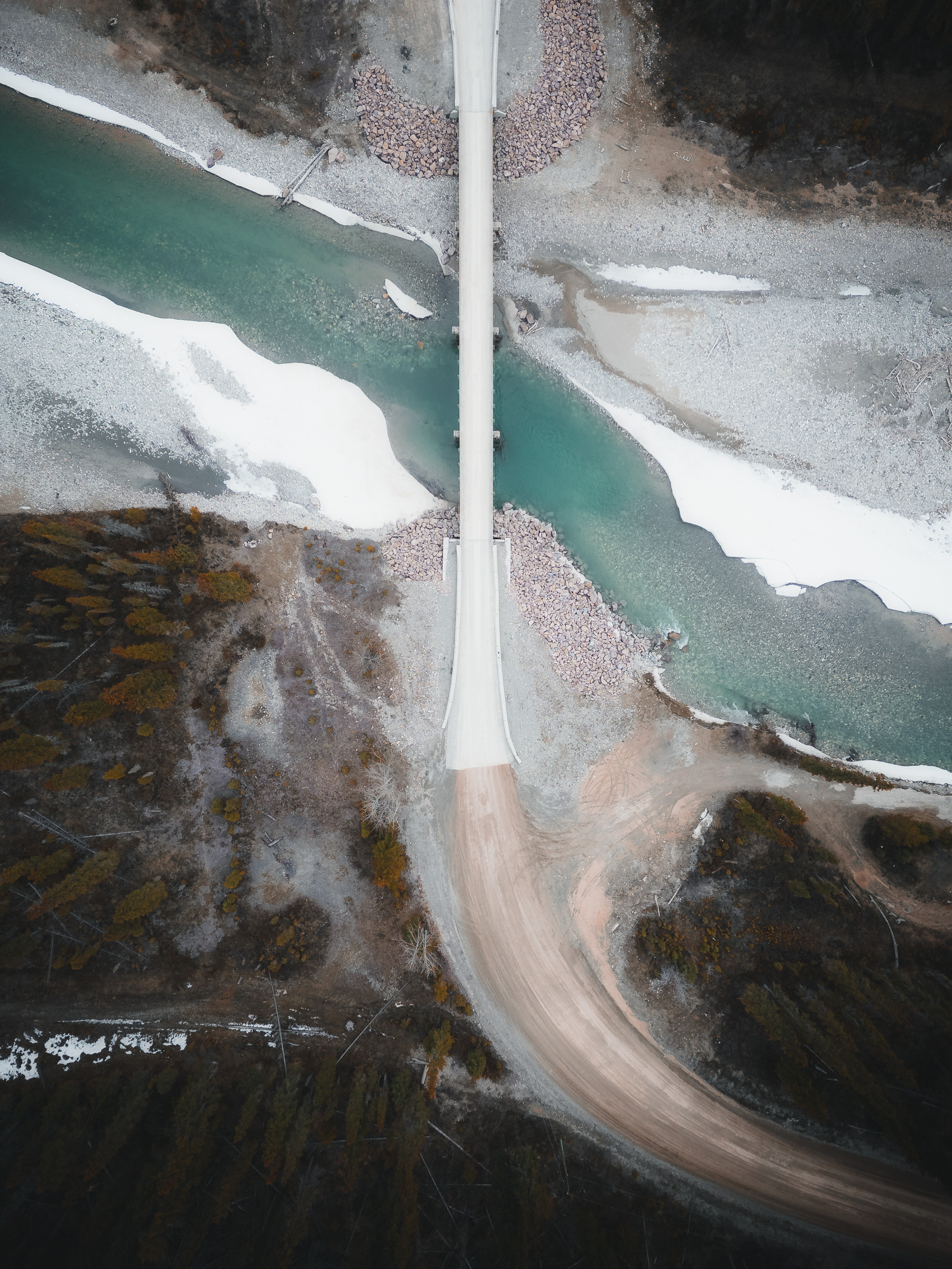 Top-down aerial view of a bridge crossing a partly frozen turquoise river