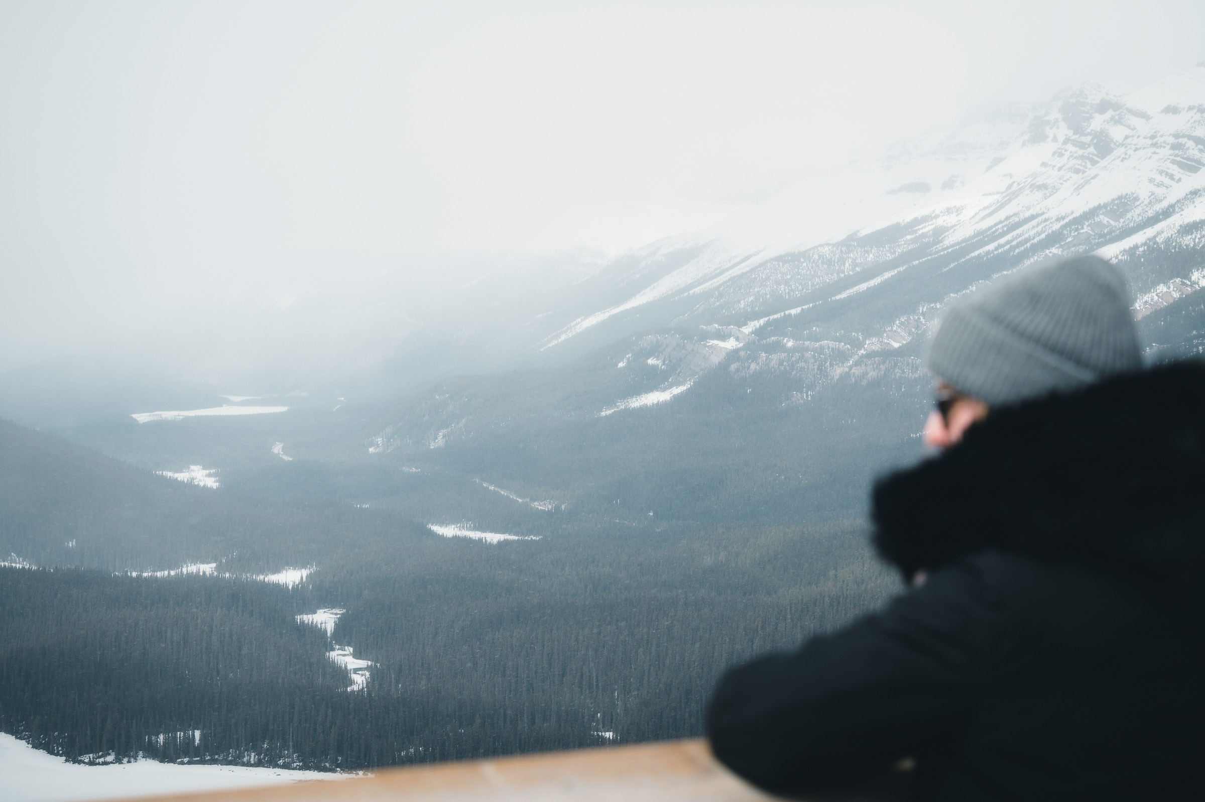 Person photographing a snowy mountain valley from a viewpoint in Canada