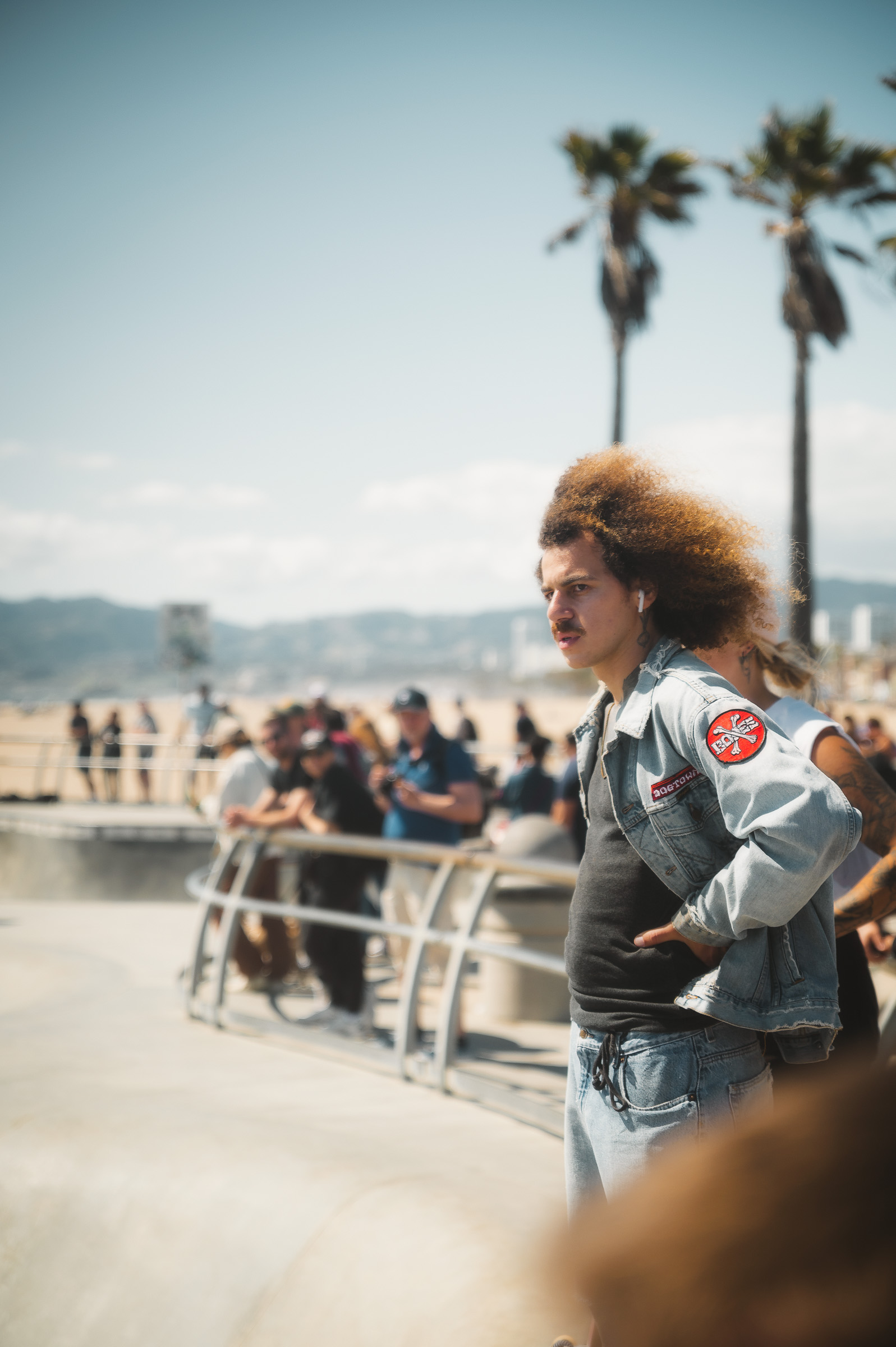 Skateboarder walking beside the crowded skatepark at Venice Beach