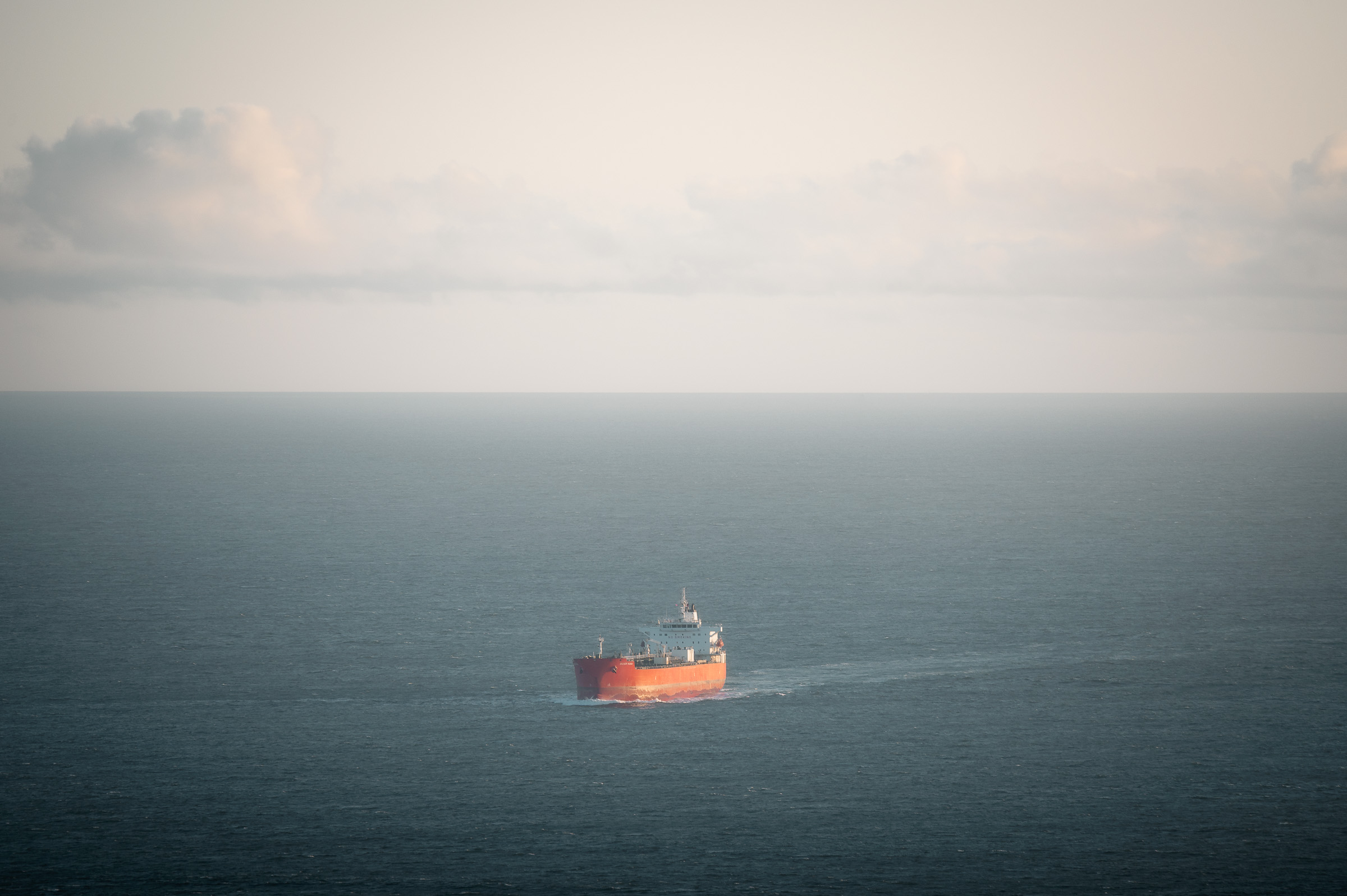 Red cargo ship crossing the open ocean beneath a pale sky