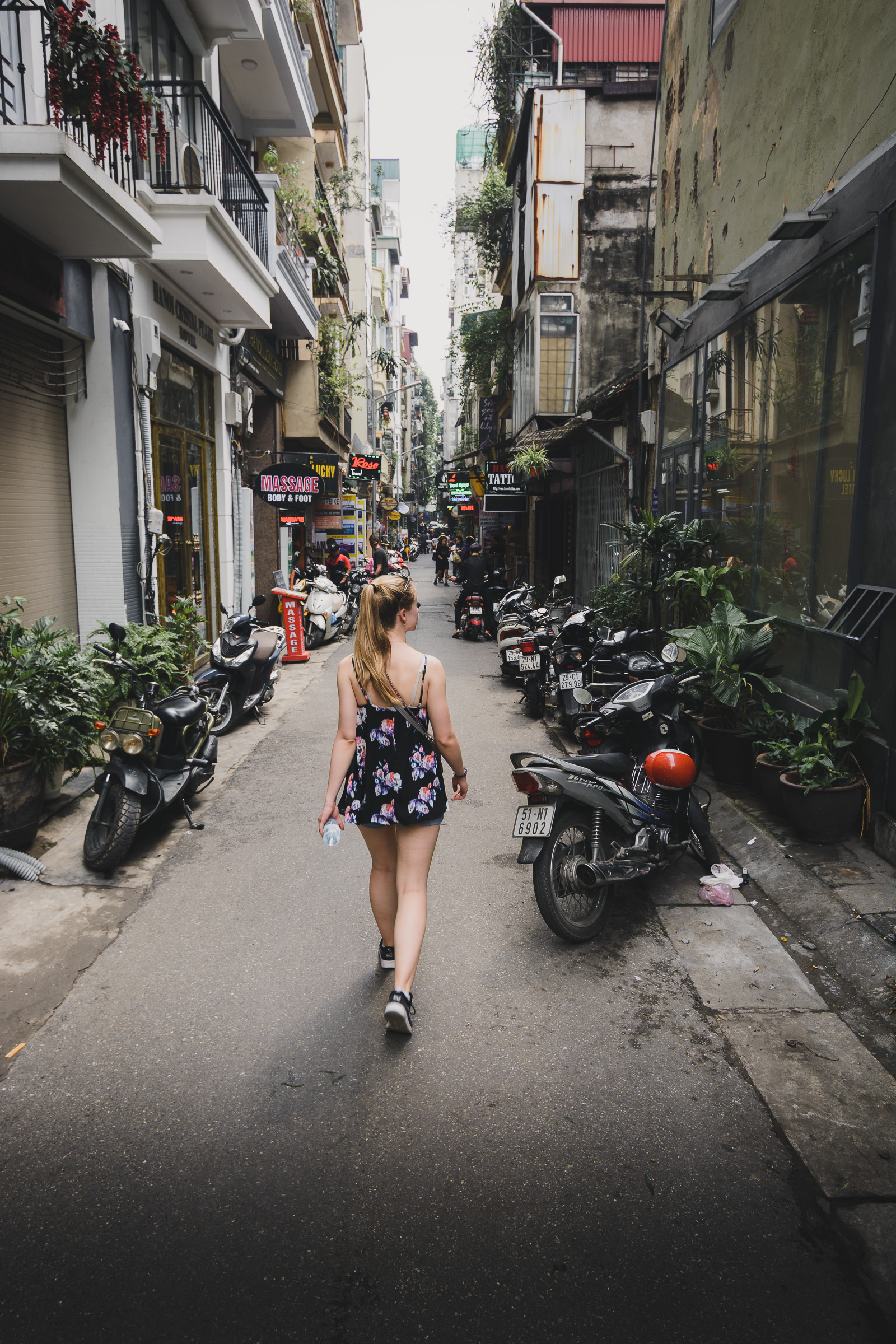 Traveler walking through a narrow Hanoi alley lined with scooters