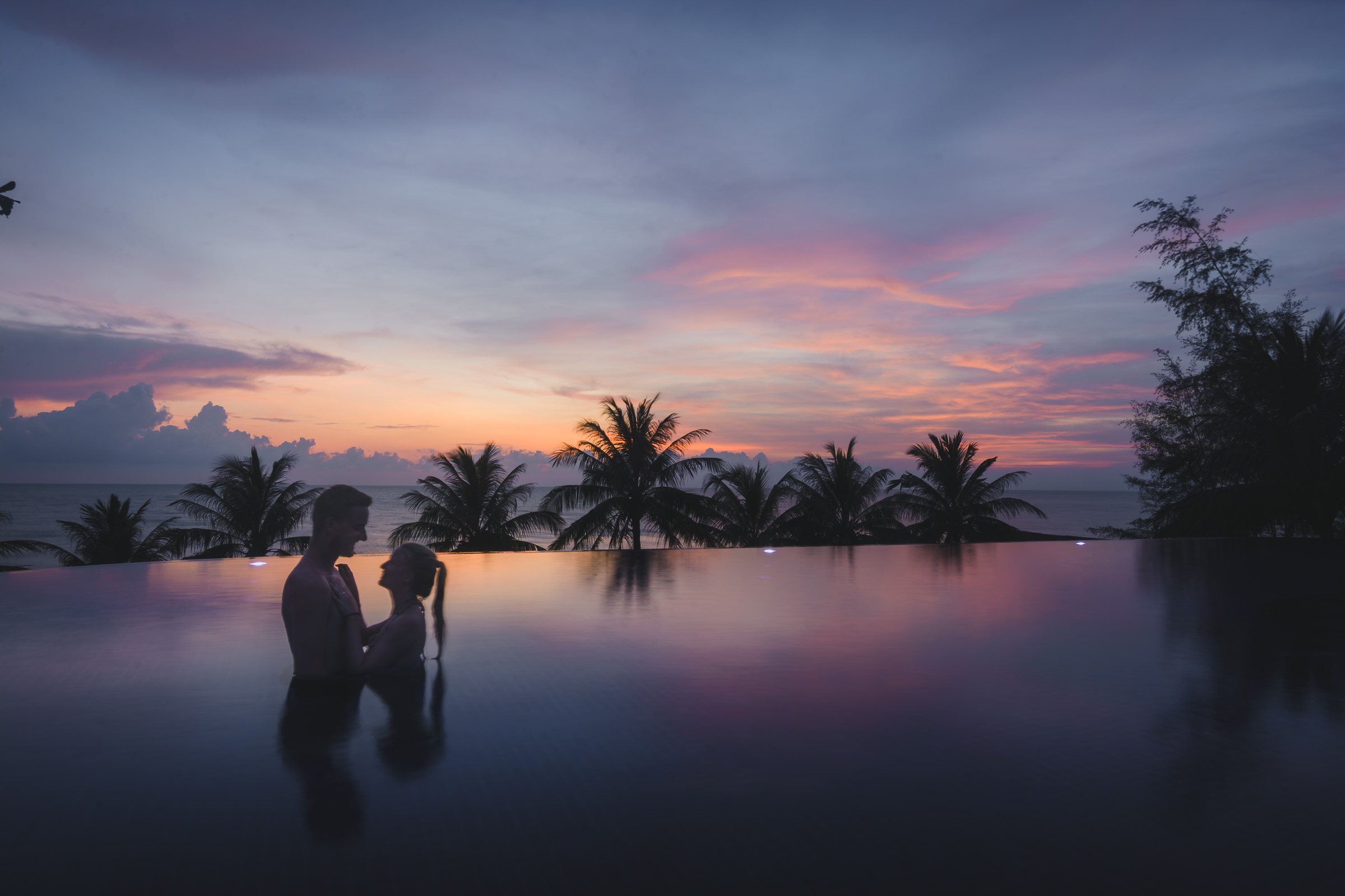 Couple standing in an infinity pool at sunset